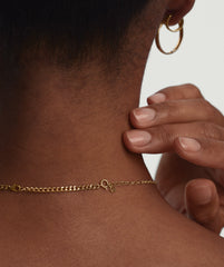Curb Chain Extender: Close-up of a gold chain on a woman's neck, with a hand gently touching a bracelet, showcasing the extender's added length.