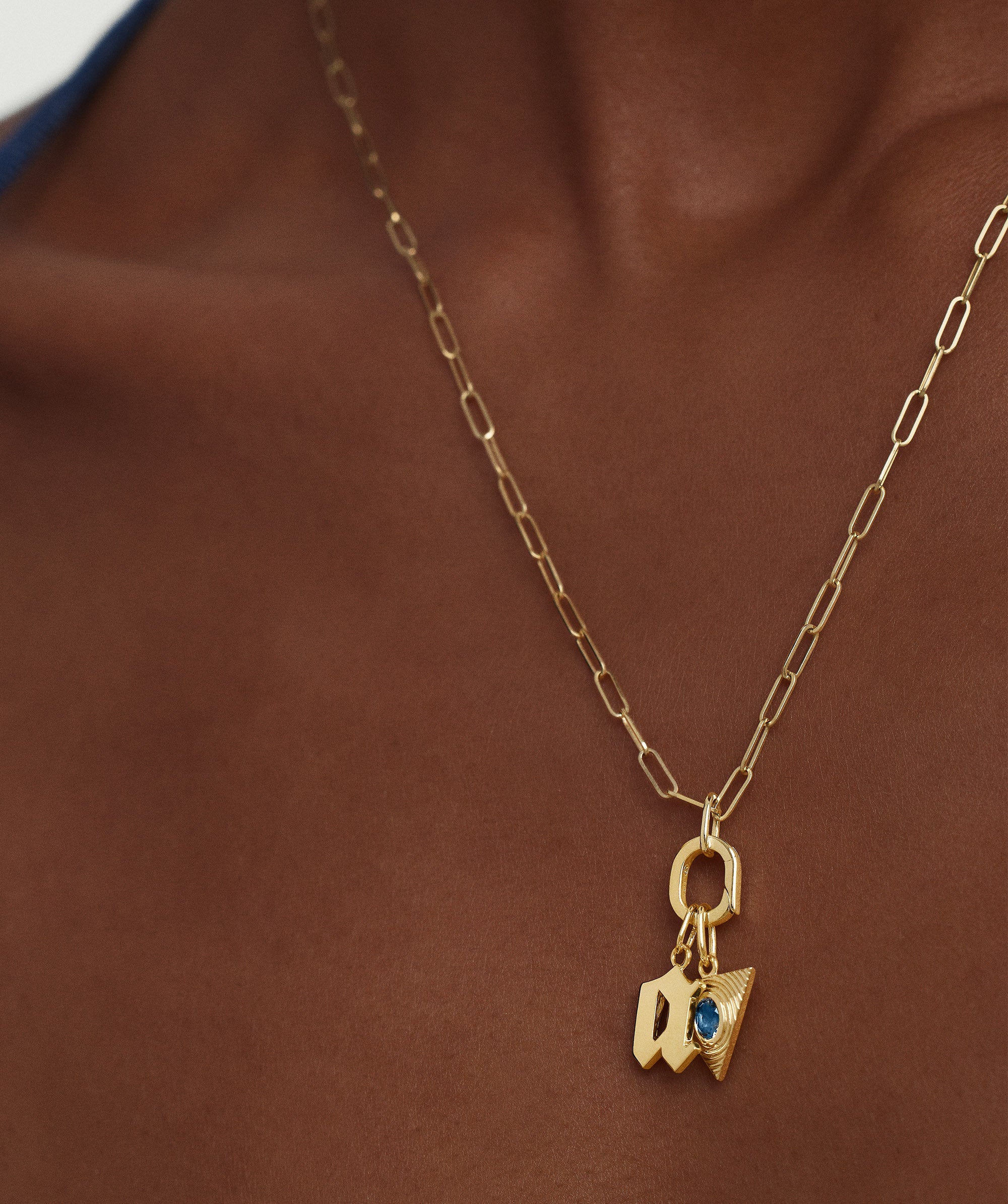 Person wearing an Oval Charm Enhancer gold necklace with a blue stone pendant, showcasing its elegant design and versatility for various styles.