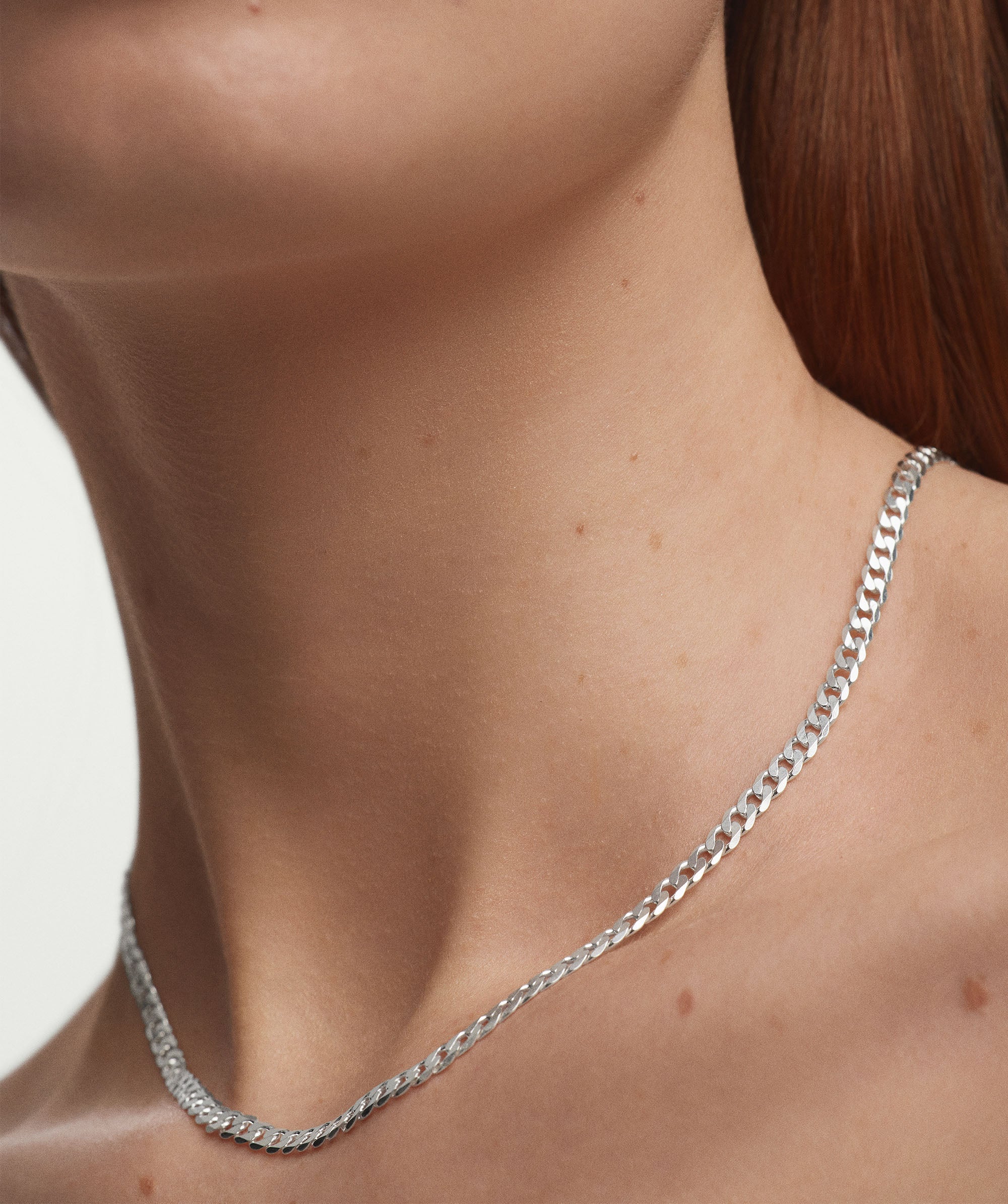 Woman wearing Flat Curb Chain Necklace, showcasing its sleek design and elegant fit around the neck.