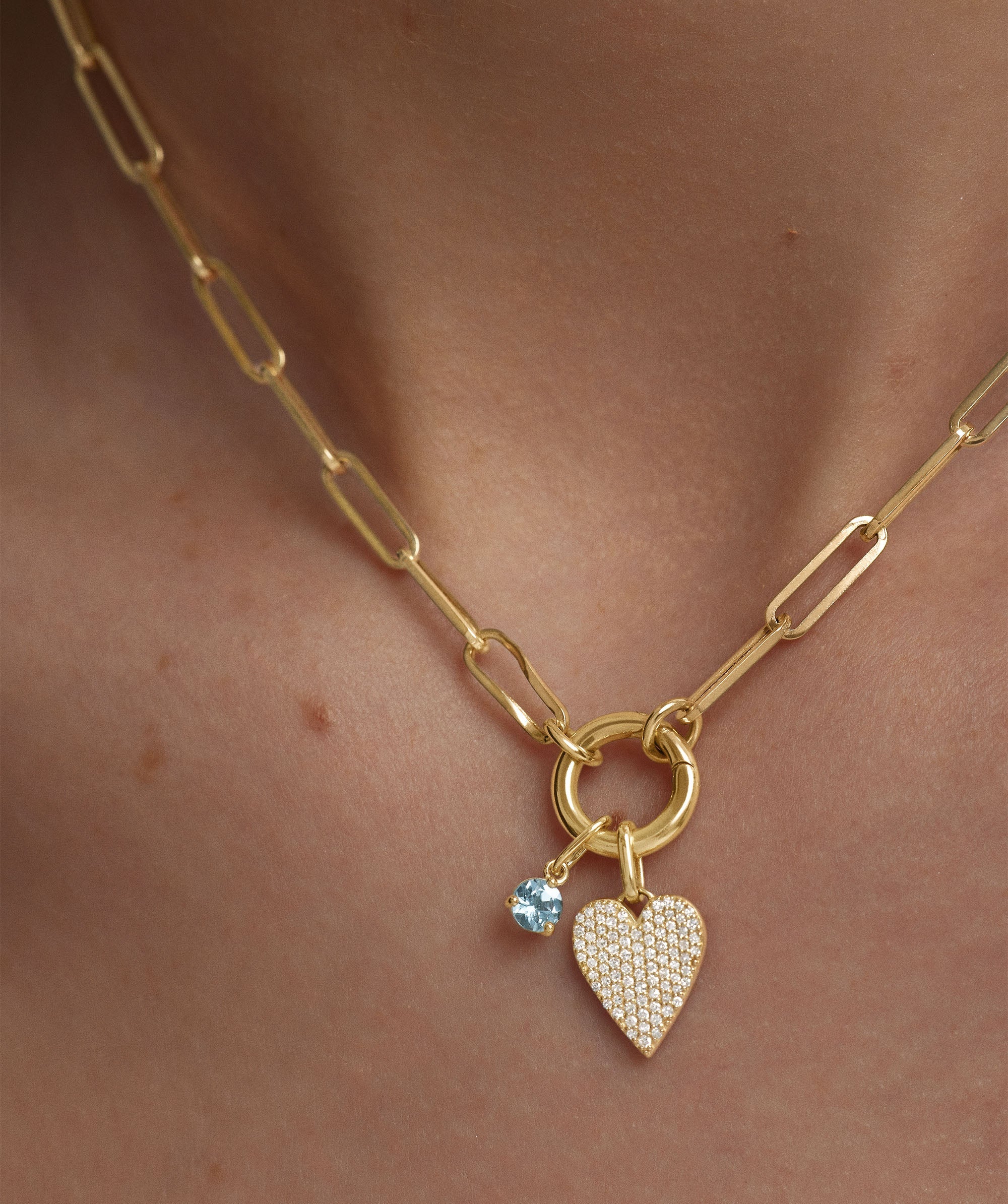PavÃ© Diamond Heart Pendant on a gold chain with a blue gemstone accent, showcased on a person.