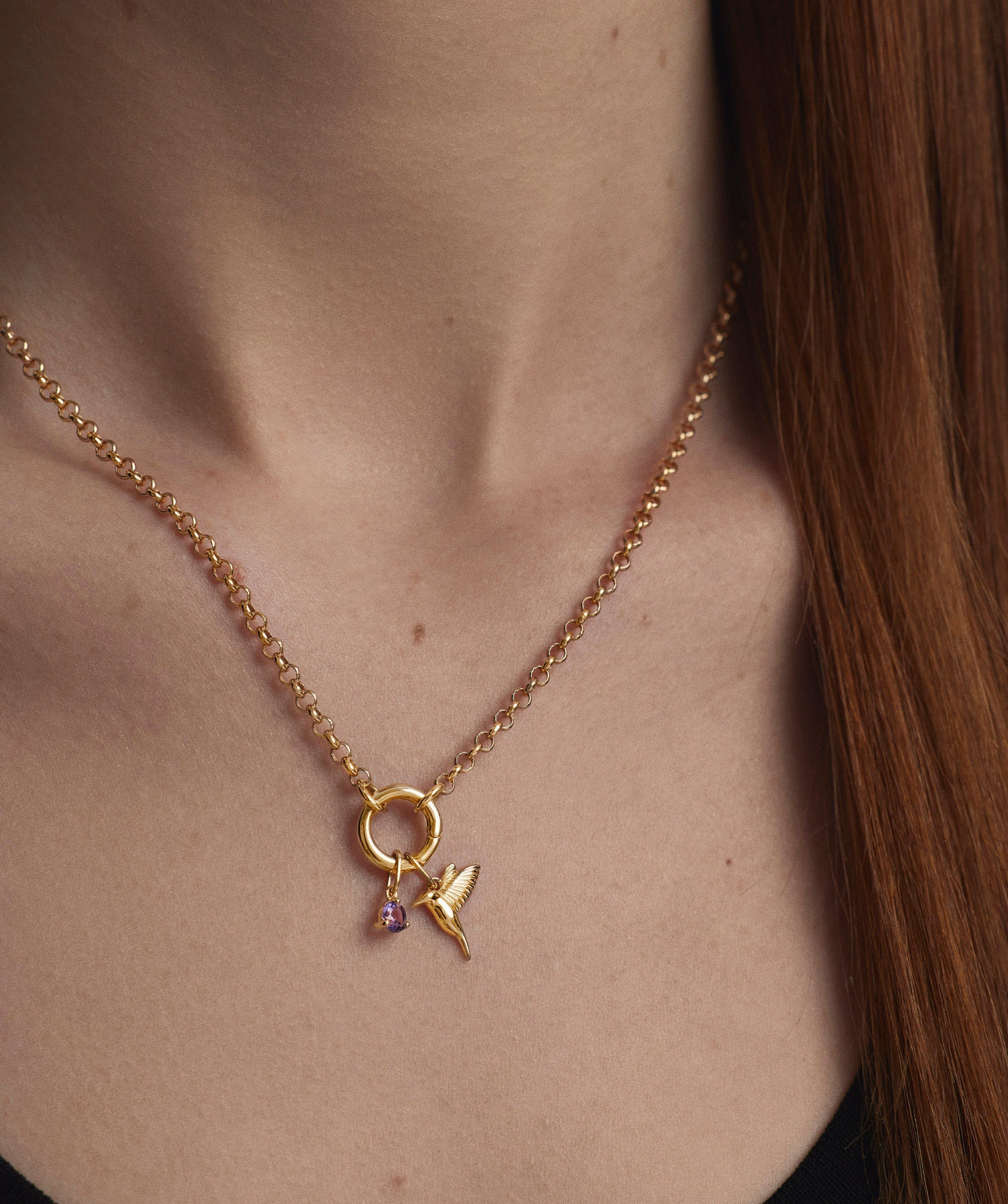 Close-up of a woman wearing a necklace with a gold hummingbird charm pendant, highlighting its elegant design and intricate detail.