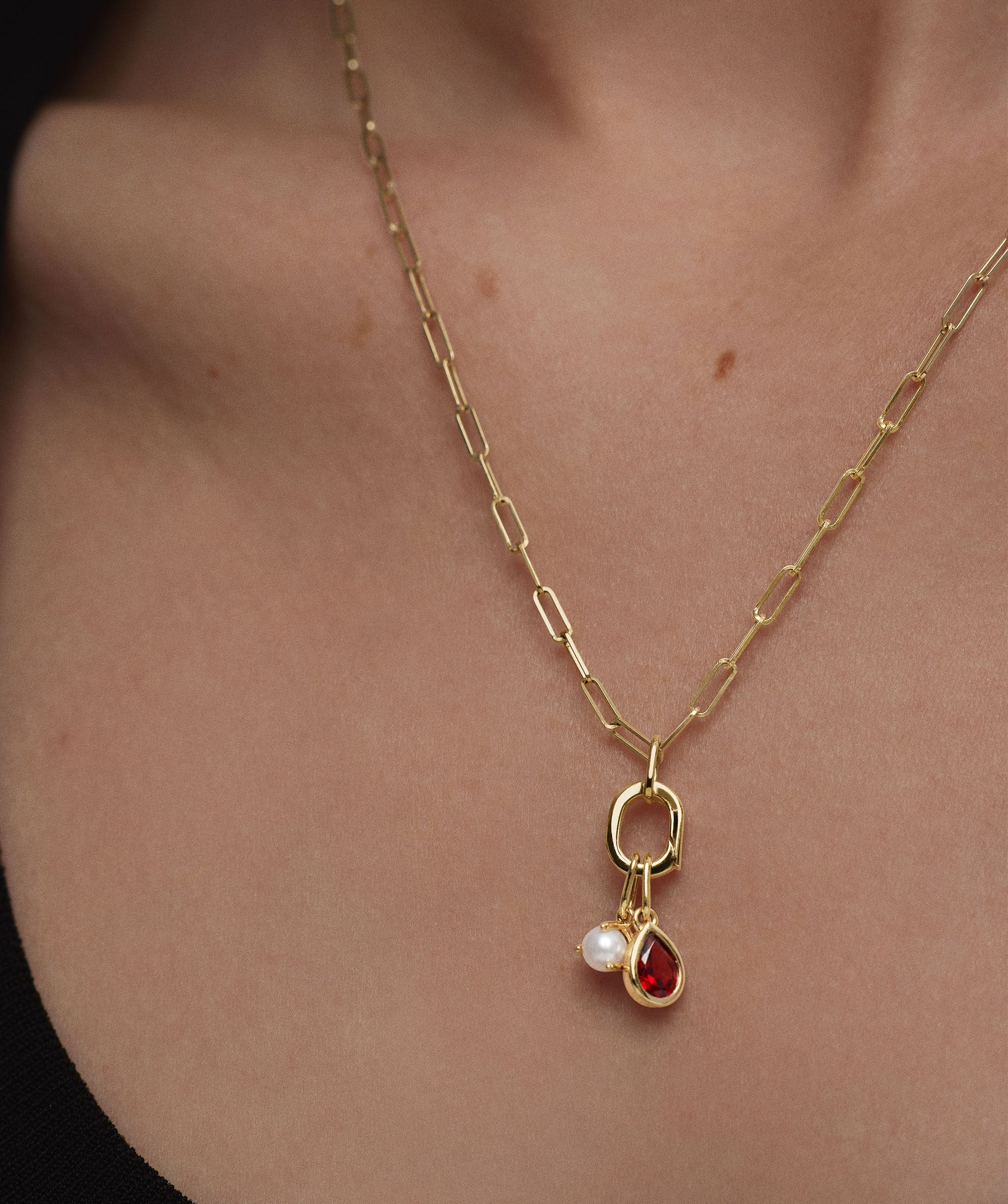 Woman wearing a Small Pear Pendant necklace featuring a gold chain with a pearl and red gem charm.