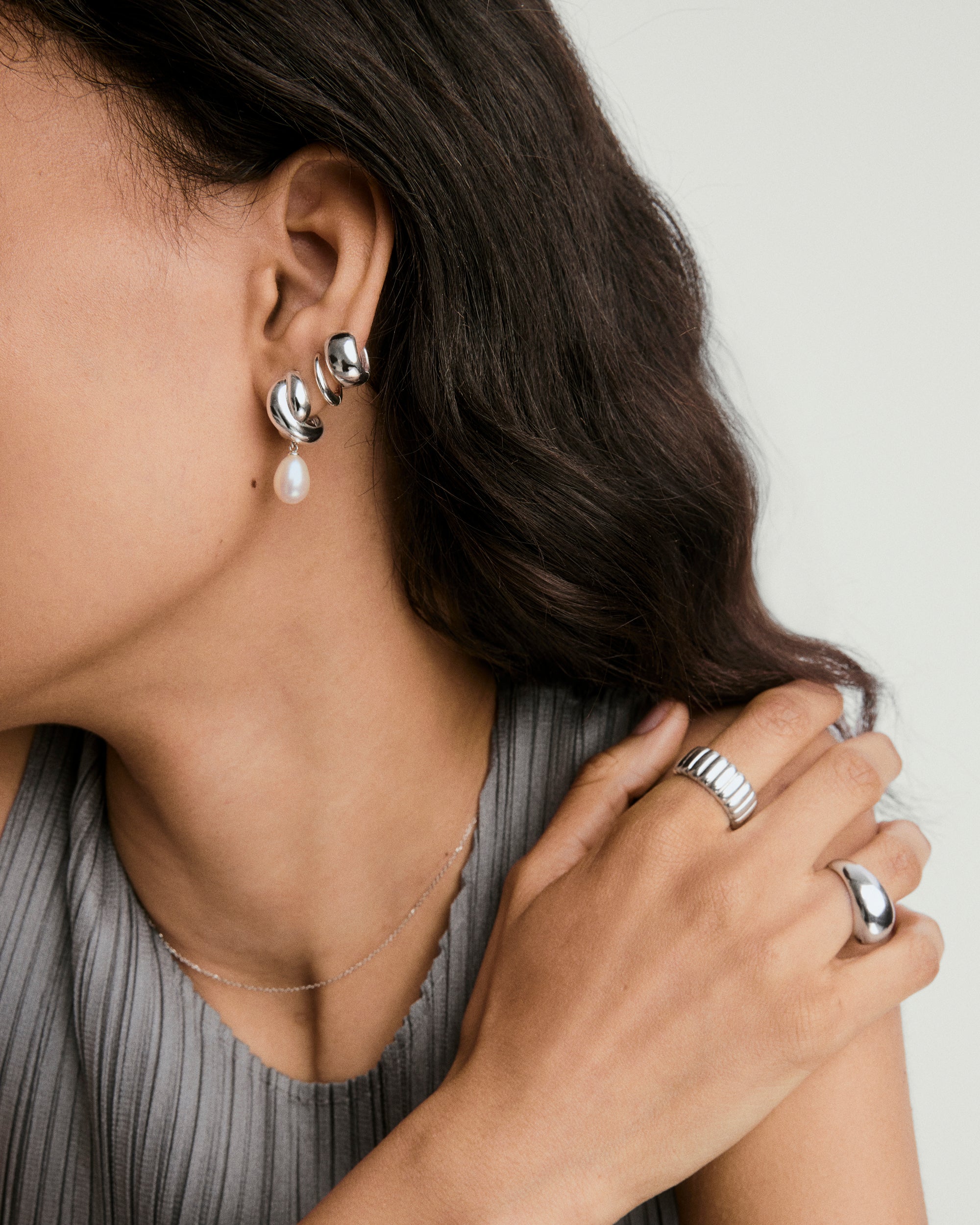 Brioche Pearl Drop Earring featuring a knot design and a dangling pearl charm, shown in a close-up on a woman's ear.