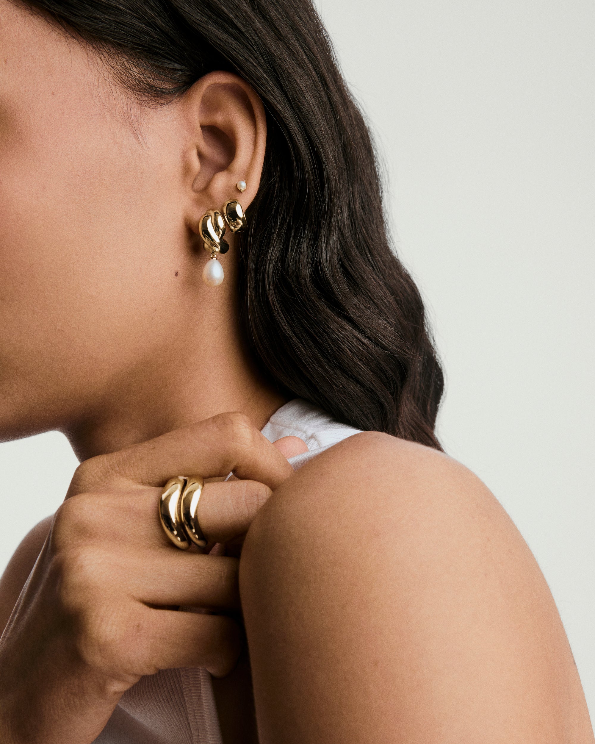 Close-up of a woman's ear wearing Brioche Pearl Drop Earring, featuring a gold hoop with a delicate pearl charm hanging elegantly.