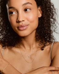 Young woman wearing the Fleurette Necklace, a delicate gold piece with a five-petal pendant and diamond accents, layered with other gold jewelry.