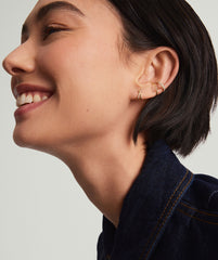 Woman smiling, showcasing PavÃ© Diamond X Studs in her ear. The 14k gold earrings feature responsibly sourced pavÃ© diamonds in an elegant overlapping tubular design.