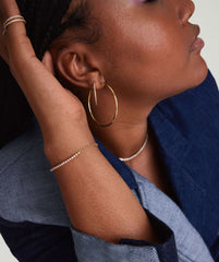 Woman wearing a Diamond Half Tennis Bracelet, handcrafted in 14k solid gold with responsibly sourced diamonds, alongside gold hoop earrings and a beaded necklace.