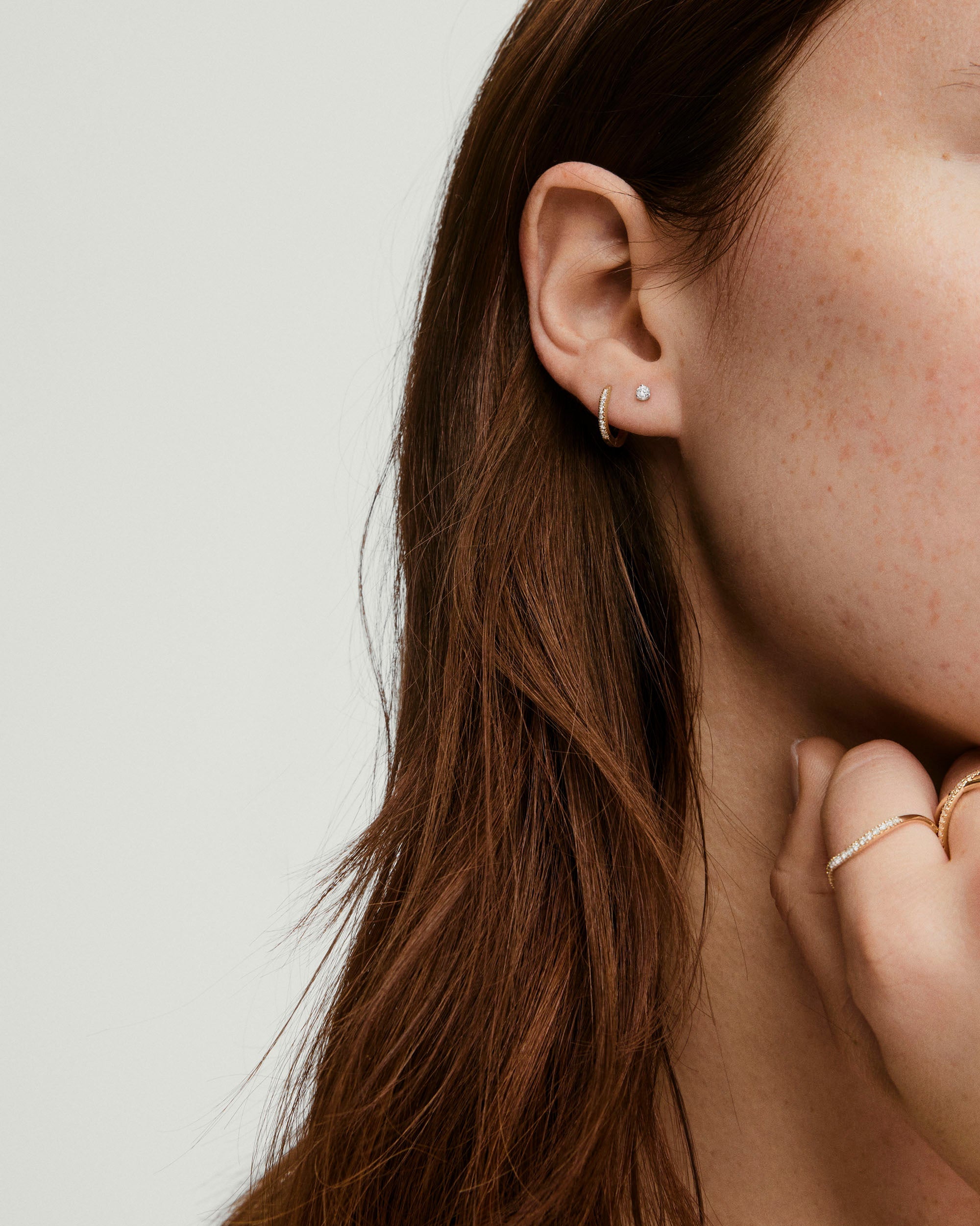 Close-up of a woman's ear showcasing the Piercing Studio - Diamond Mini Flat Back Stud, a 14k gold stud with titanium backing for comfort and healing.