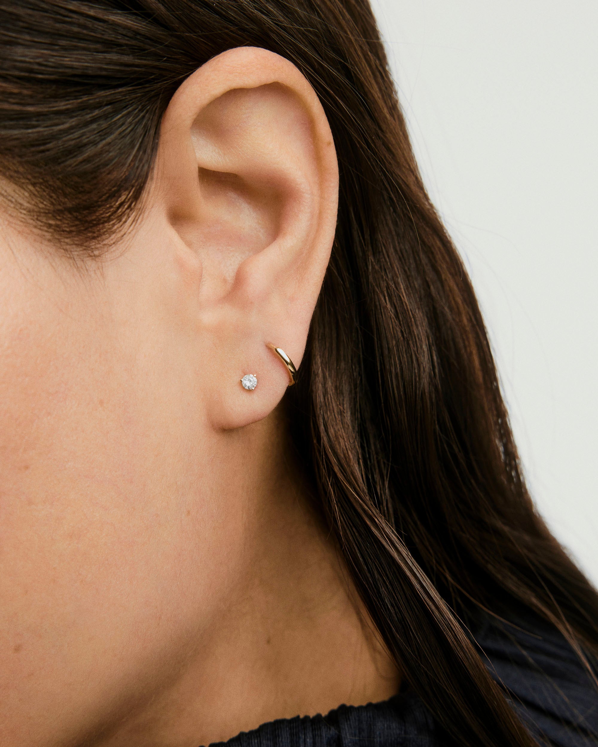 Diamond Mini Stud earring displayed on a woman's ear, highlighting its elegant, simple design, perfect for mixing and matching with other basic studs.