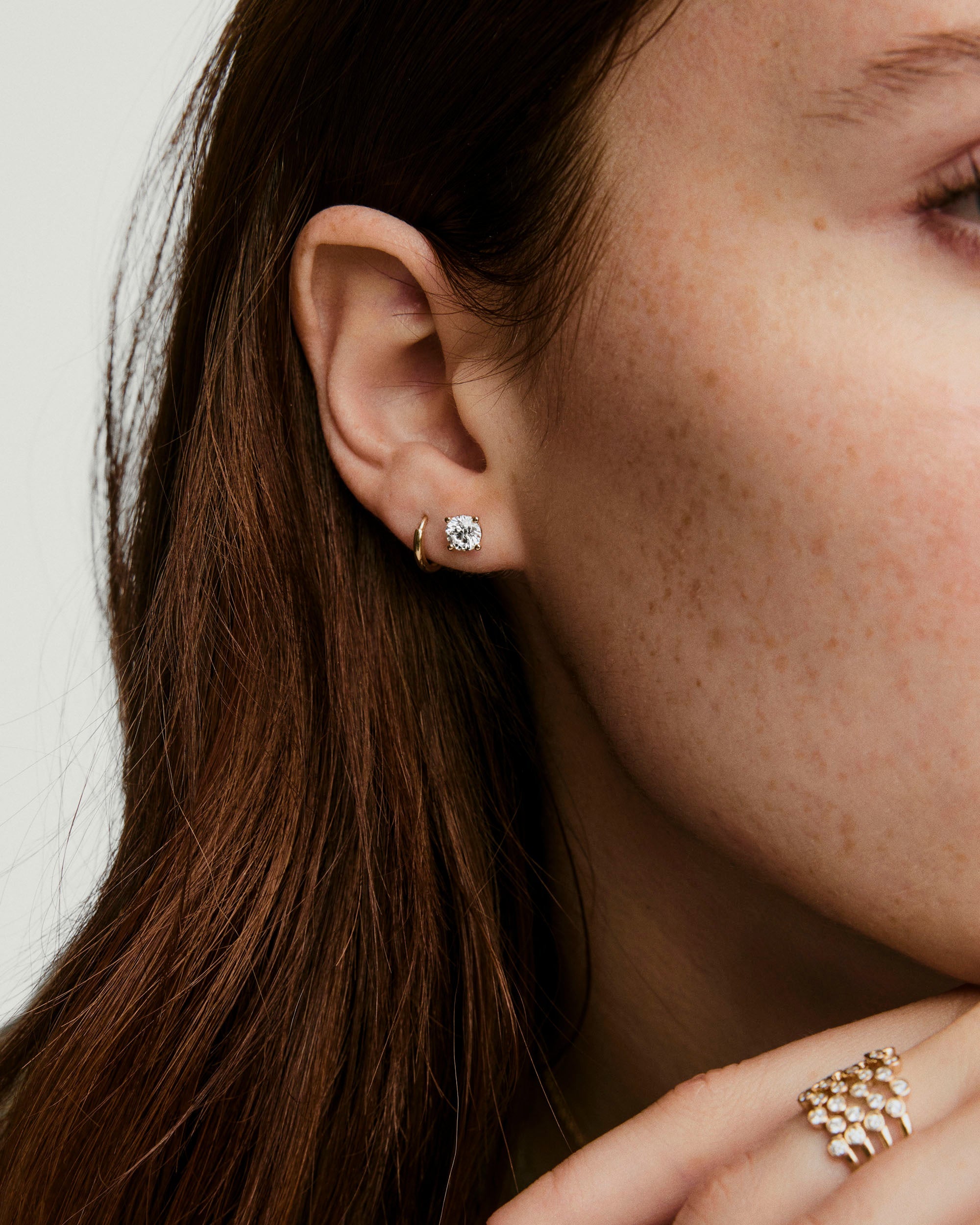 Lab Grown Diamond Round Studs 1 TCW on a woman's ear, showcasing the brilliant sparkle of the lab-grown diamonds set in 14k solid gold.