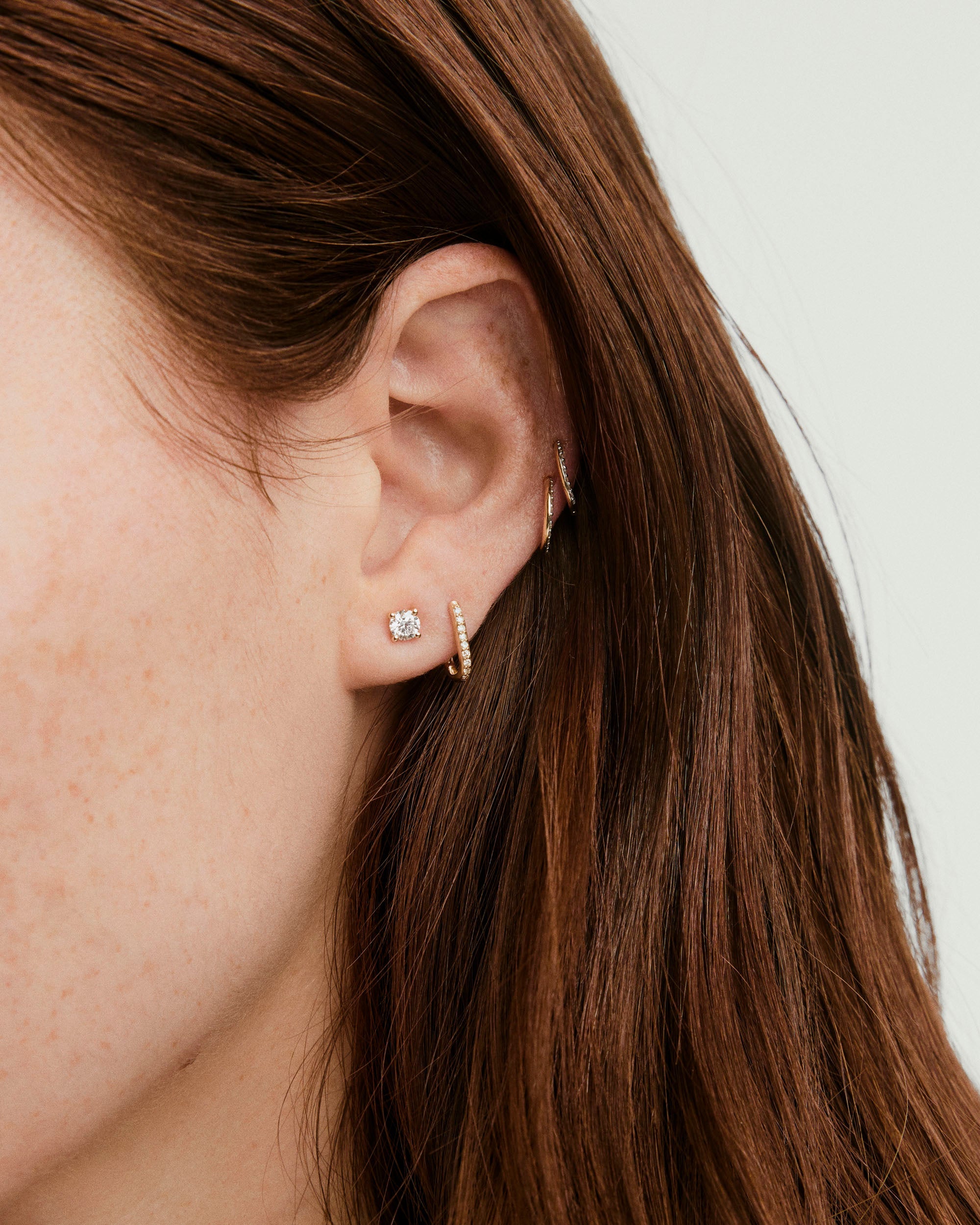 Close-up of a woman's ear adorned with large diamond studs, showcasing a handcrafted, unique diamond setting for timeless elegance.