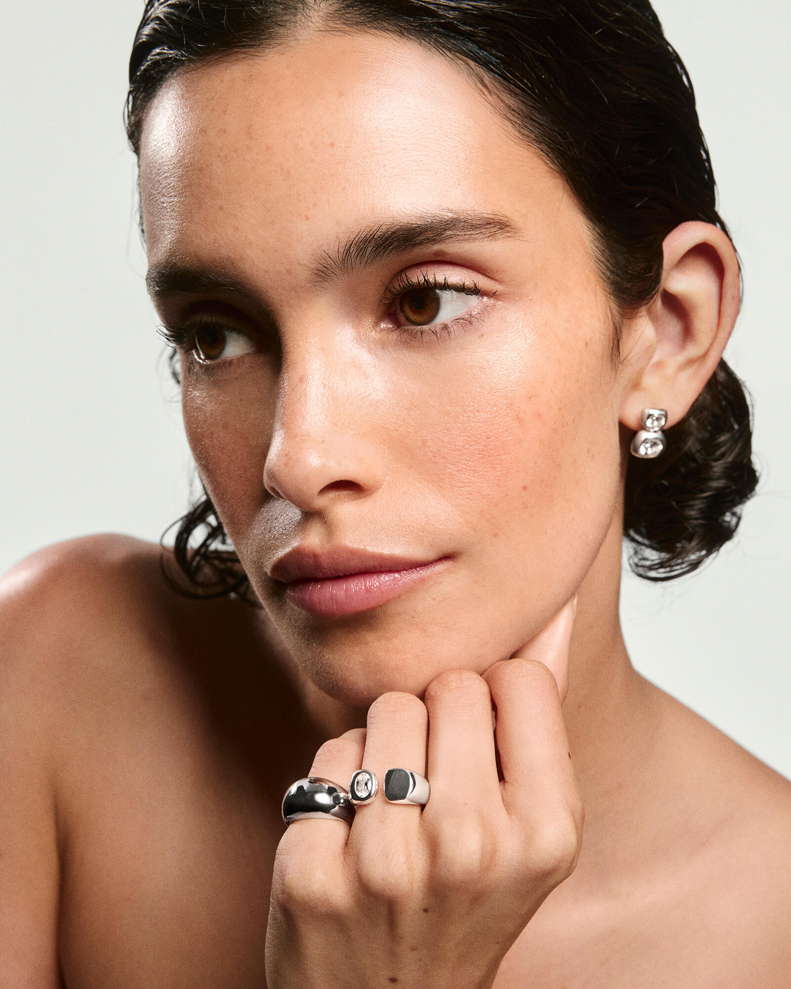 Young woman with slicked-back hair wearing Noa Open Signet Pinky Ring featuring a gemstone on an open-faced band, alongside other chunky silver rings and a small earring.