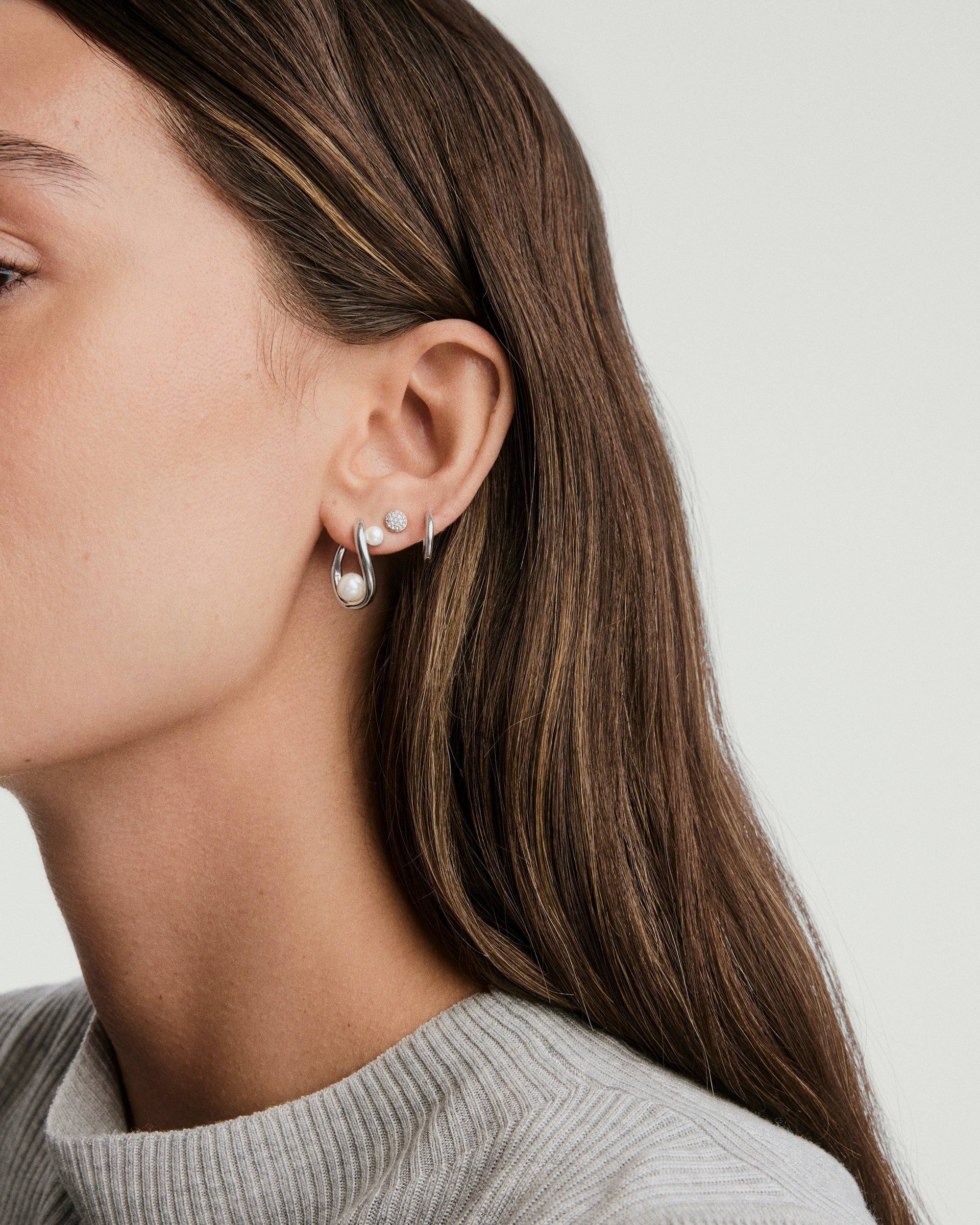 Close-up of a woman's ear wearing DÃ´me Figure Pearl Hoops, showcasing interwoven pearls of various sizes, highlighting the earring's intricate design and elegance.