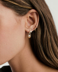 Close-up of a woman's ear wearing DÃ´me Figure Pearl Hoops, showcasing interwoven pearls of varying sizes in gold hoop earrings.