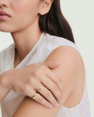 A woman's hand showcases the DÃ´me Figure Slim Ring, a gold band with fluid curves set with small diamonds, exemplifying minimalist, modern jewelry styling.