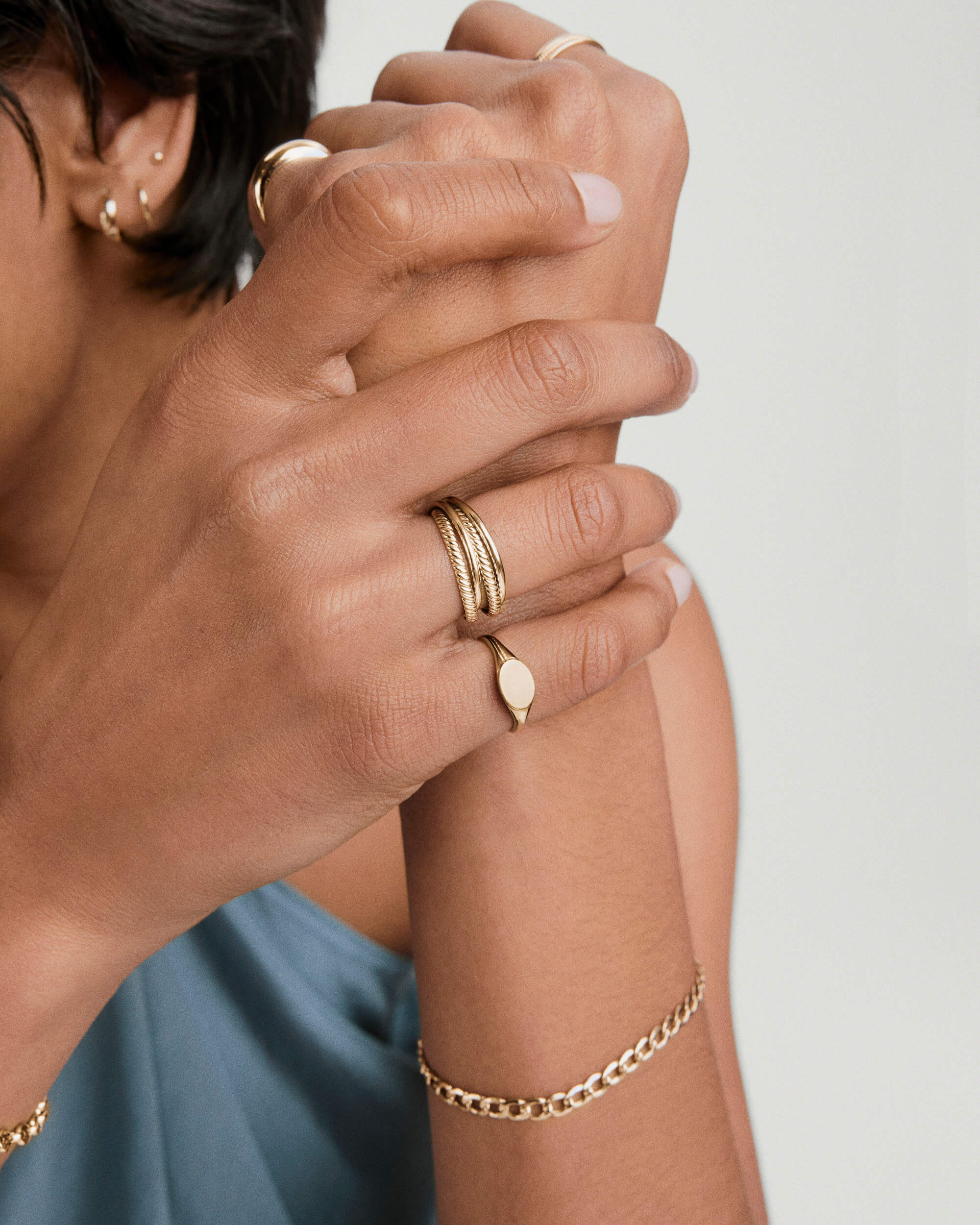Hands adorned with gold jewelry, highlighting the Duo Ringâa handcrafted 14k solid gold piece with two thicker bands, elegantly worn on the right index finger.