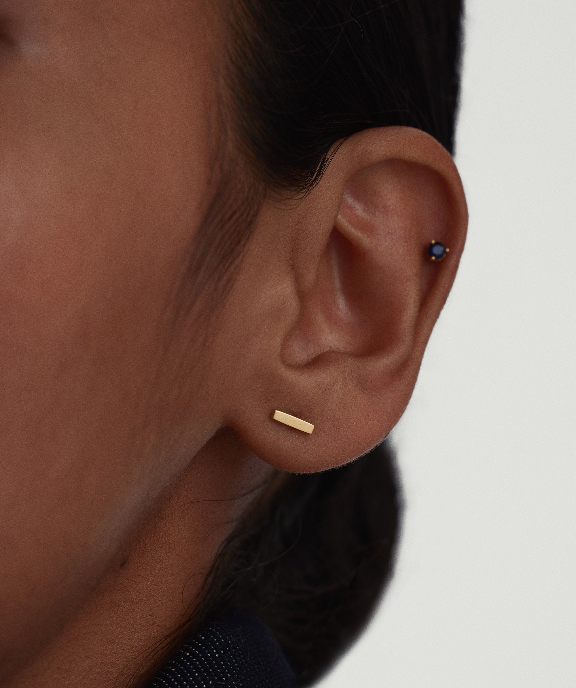 Piercing Studio - Bar Flat Back Stud showcased near an ear, highlighting its sleek, classic design perfect for stacking with other earrings.