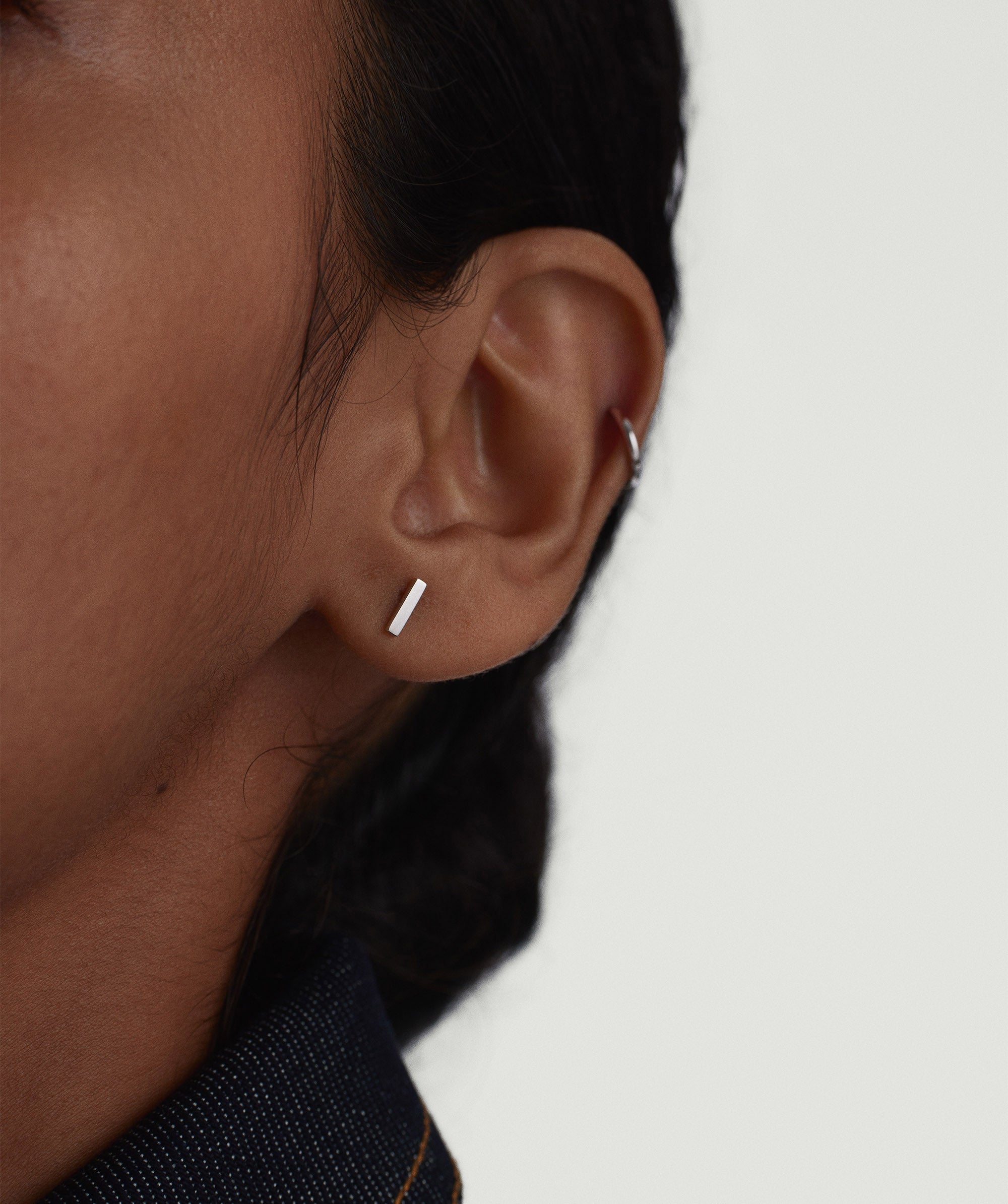 Close-up of a woman's ear wearing Piercing Studio - Bar Flat Back Stud, a sleek silver square earring, highlighting its simplicity and classic design.