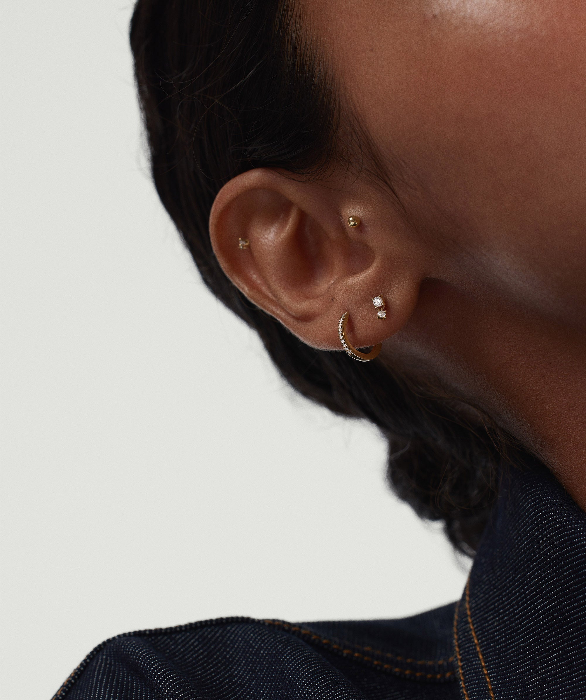 Close-up of a woman's ear wearing the Piercing Studio - Diamond Droplet Stud, showcasing a delicate, gold earring with a diamond accent.