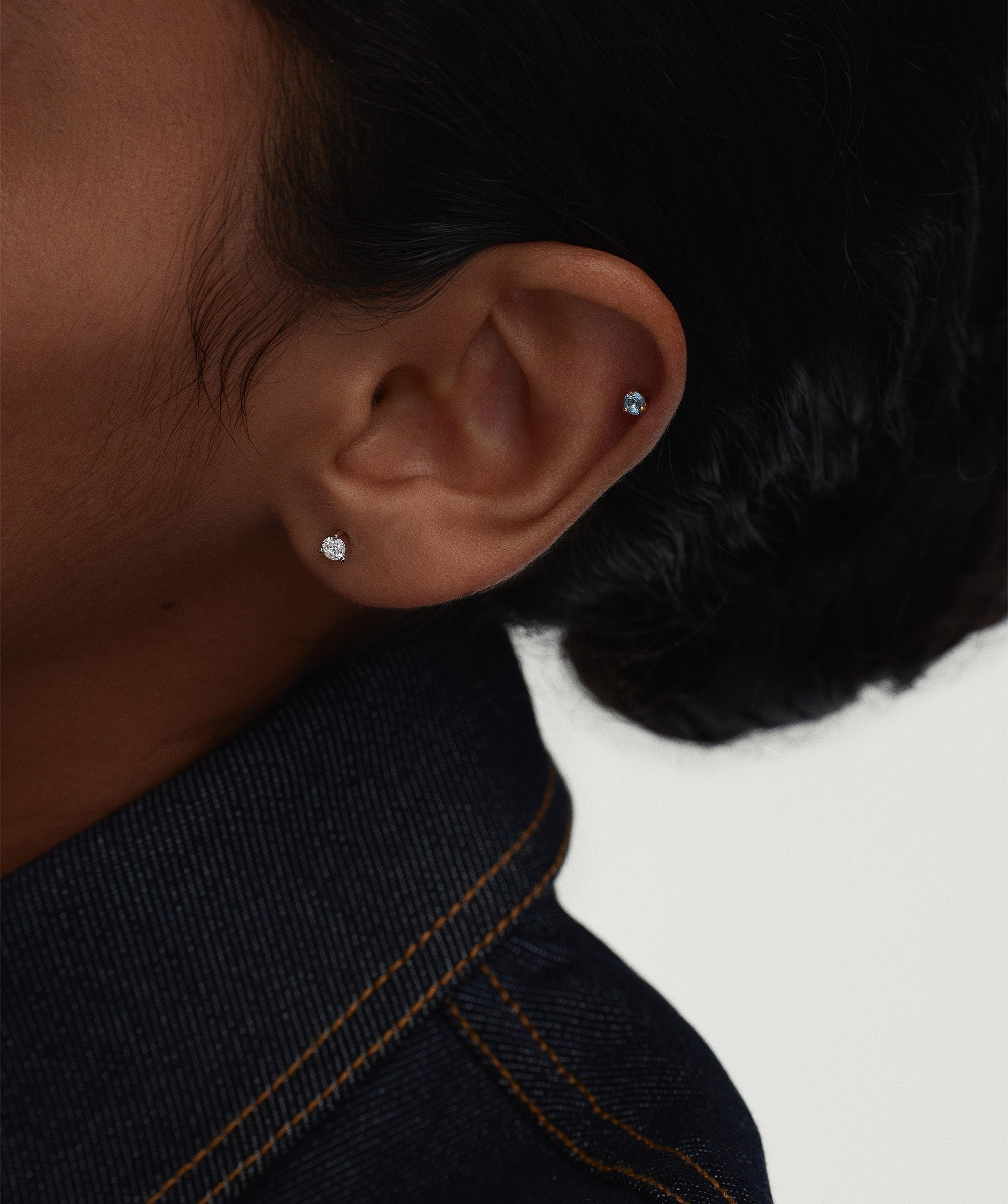 Close-up of a person's ear wearing the Piercing Studio - Round Diamond Flat Back Stud, highlighting its simplicity and elegance in a stacked earring style.