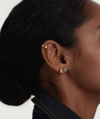 Close-up of a woman's ear wearing Piercing Studio's Turquoise Diamond Droplet Flat Back Stud, showcasing the elegant gold earrings as a fashion accessory.