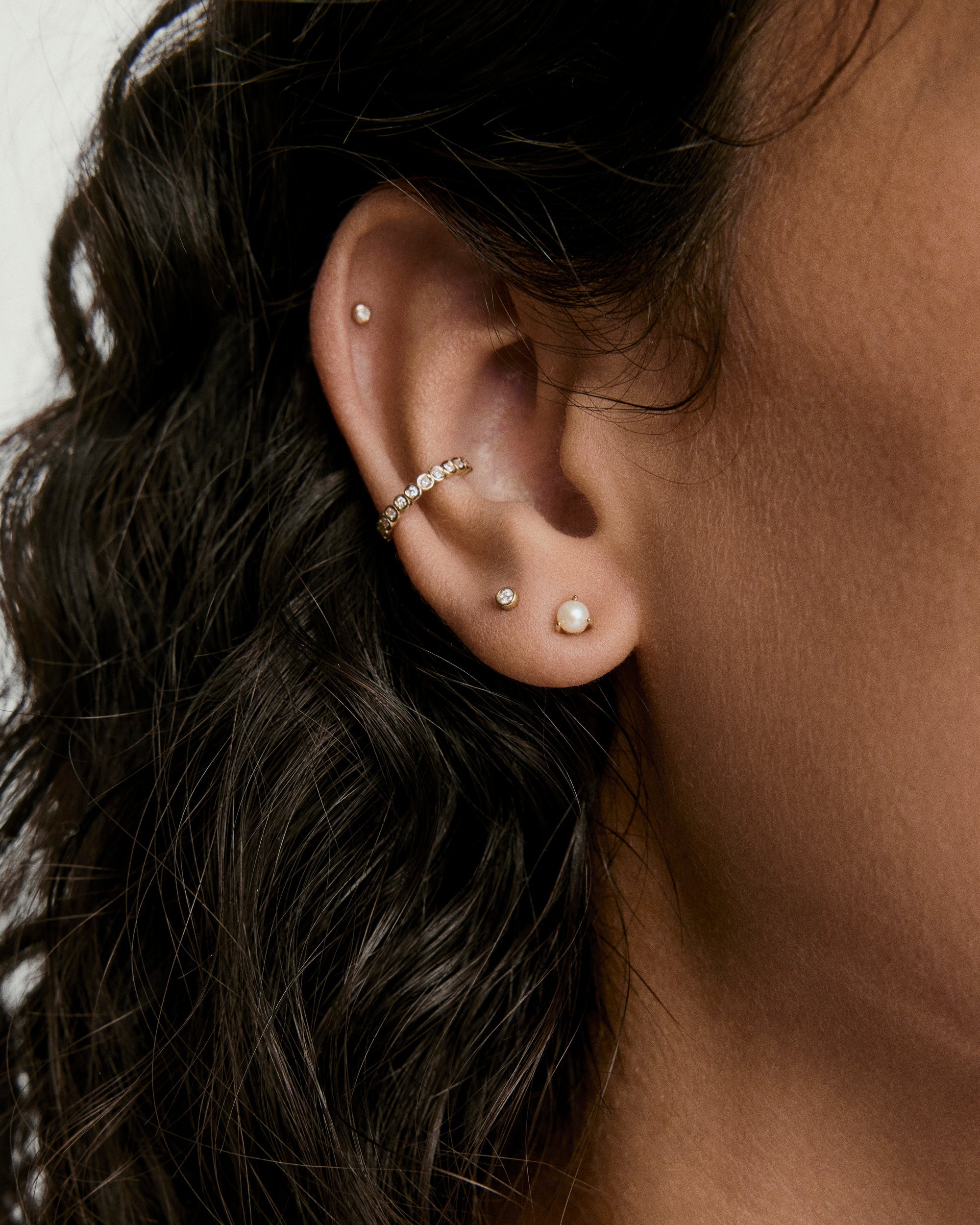 Tiny Diamond Stud adorning a woman's ear; bezel-set for a subtle shine, flat back design ensures comfort for all-day wear.