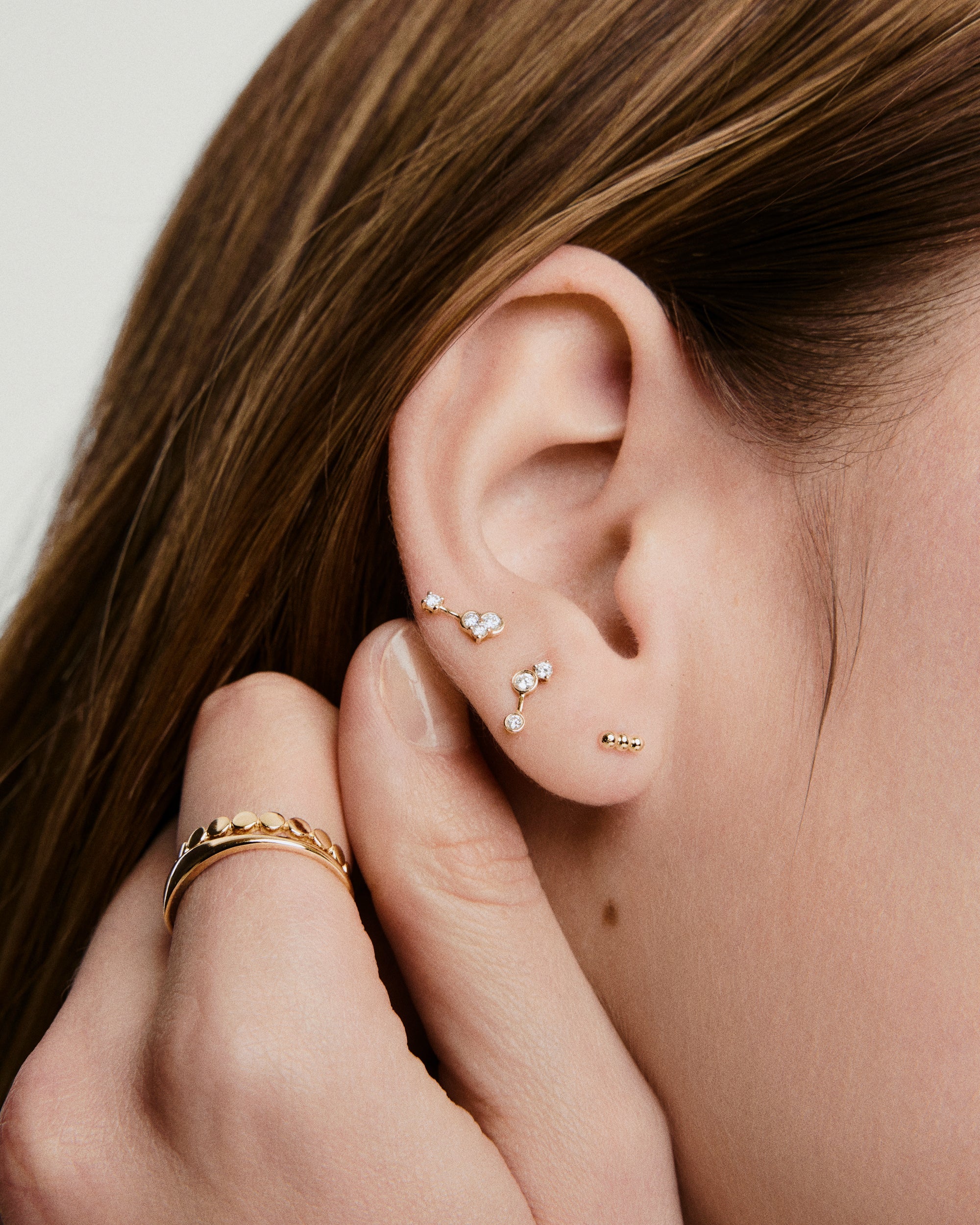 Spheres Bar Stud showcased on a woman's ear, featuring three gold spheres forming a versatile bar design, perfect for stacking and comfortable all-day wear.