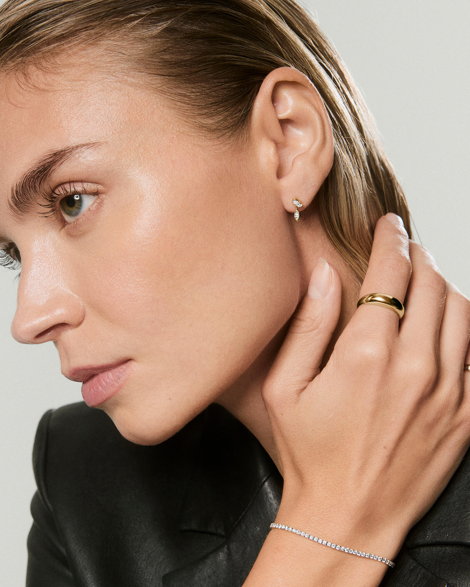 Profile view of a woman wearing Piercing Studio - Lab Grown Diamond Drop Studs, showcasing their elegant sparkle alongside a gold band and diamond tennis bracelet.