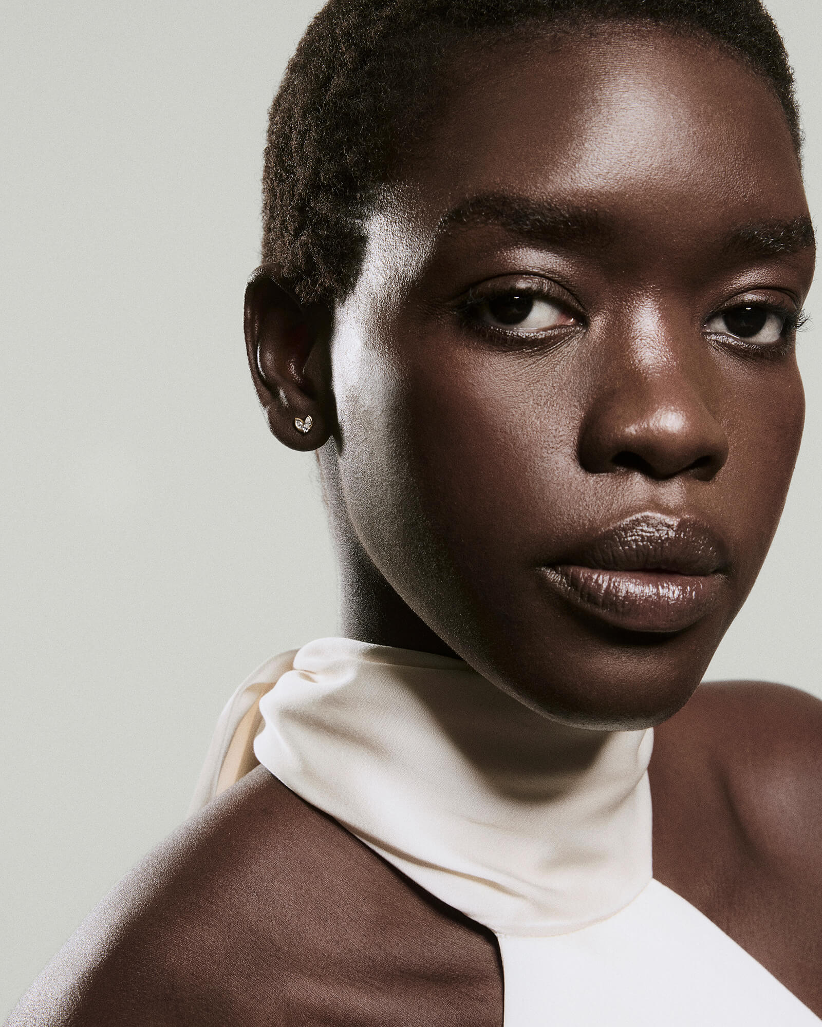 Person with short hair wears Piercing Studio - Lab Grown Diamond Petal Stud, showcasing minimalist elegance with subtle, triple-diamond design against smooth skin and simple attire.