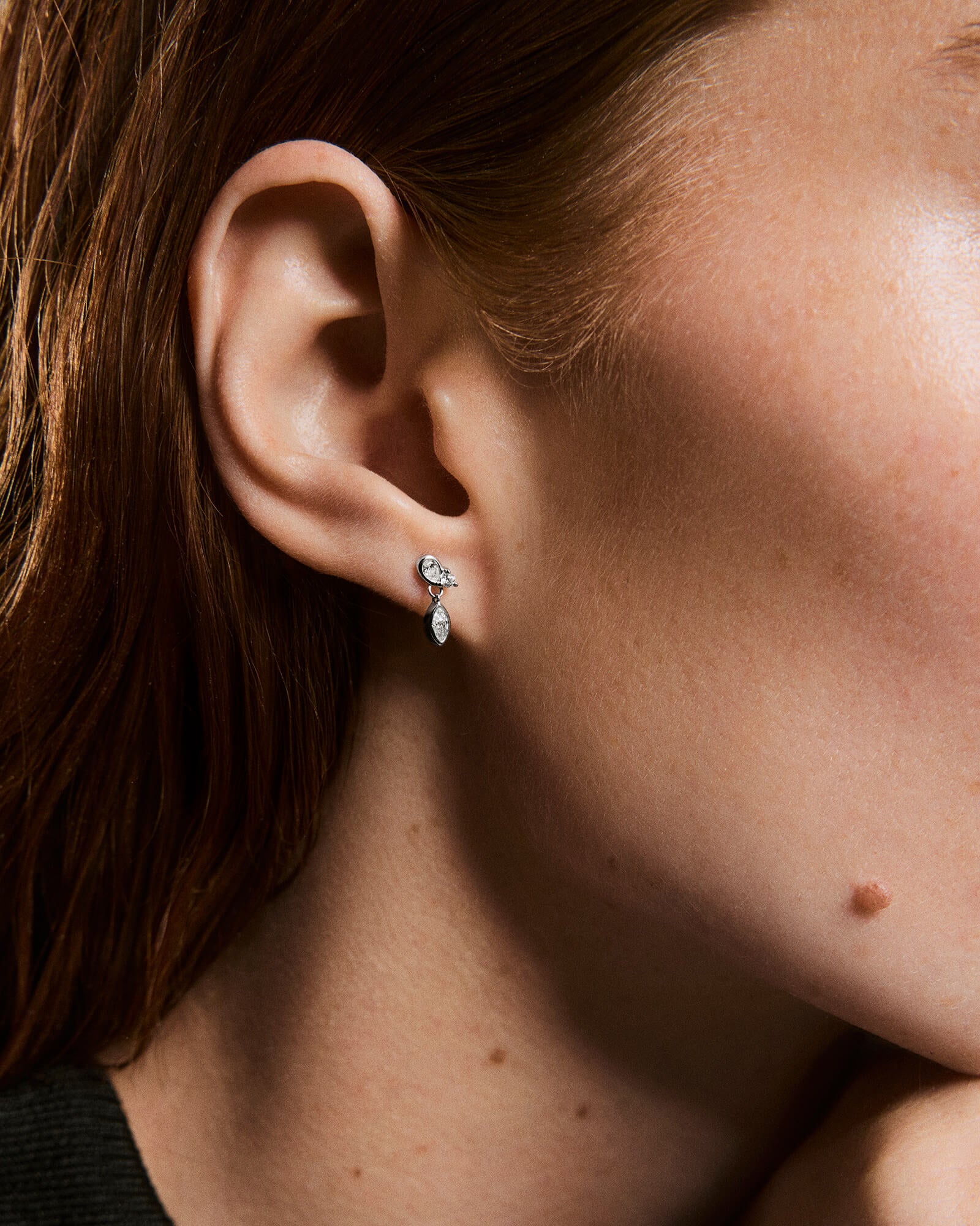 Close-up of a left ear wearing Piercing Studio - Lab Grown Diamond Drop Studs, featuring a round stud with a hanging marquise-shaped stone.