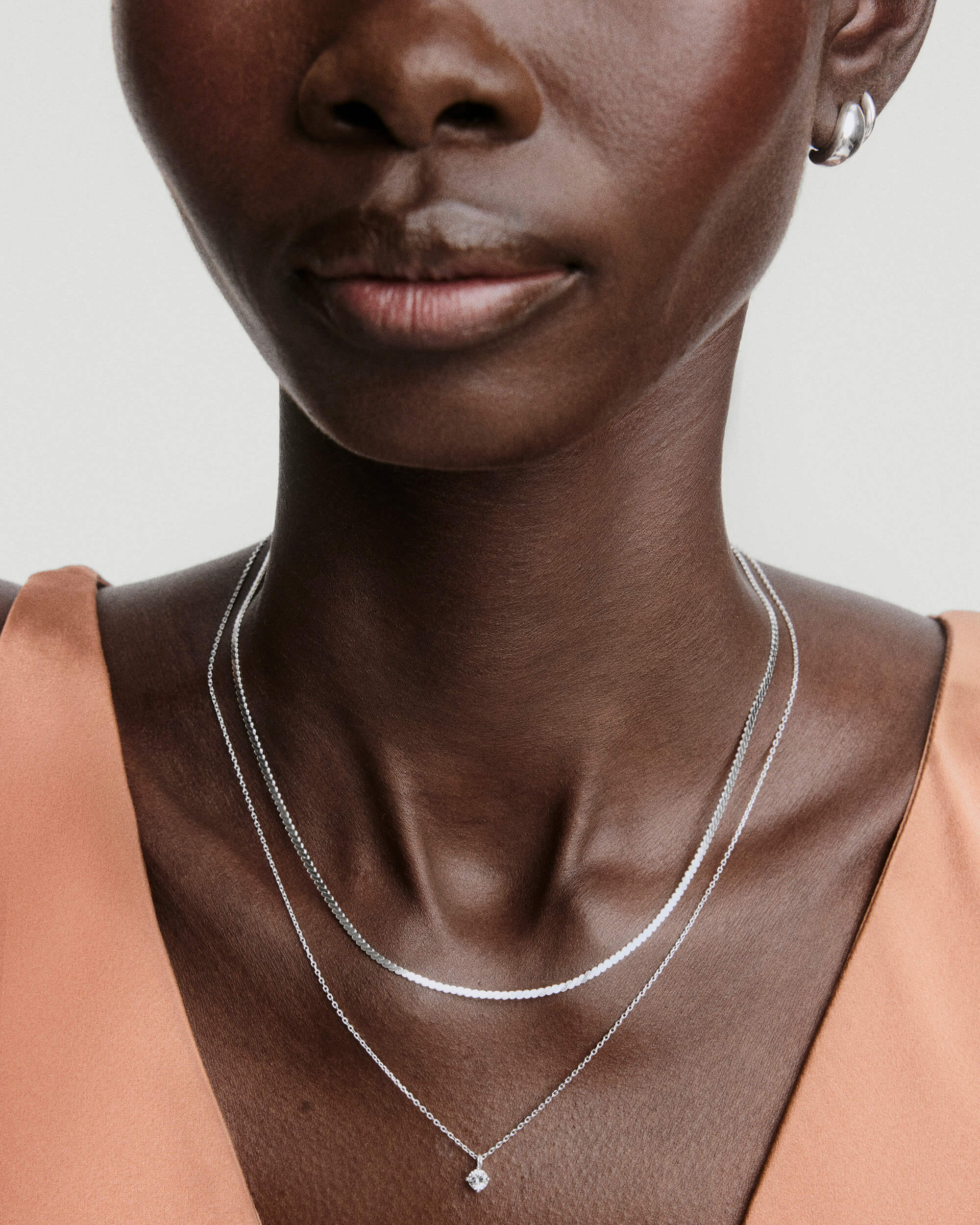 Lab Grown Sapphire Necklace Bundle shown on dark skin, featuring a layered silver snake chain and a pendant necklace, paired with small silver hoop earrings.