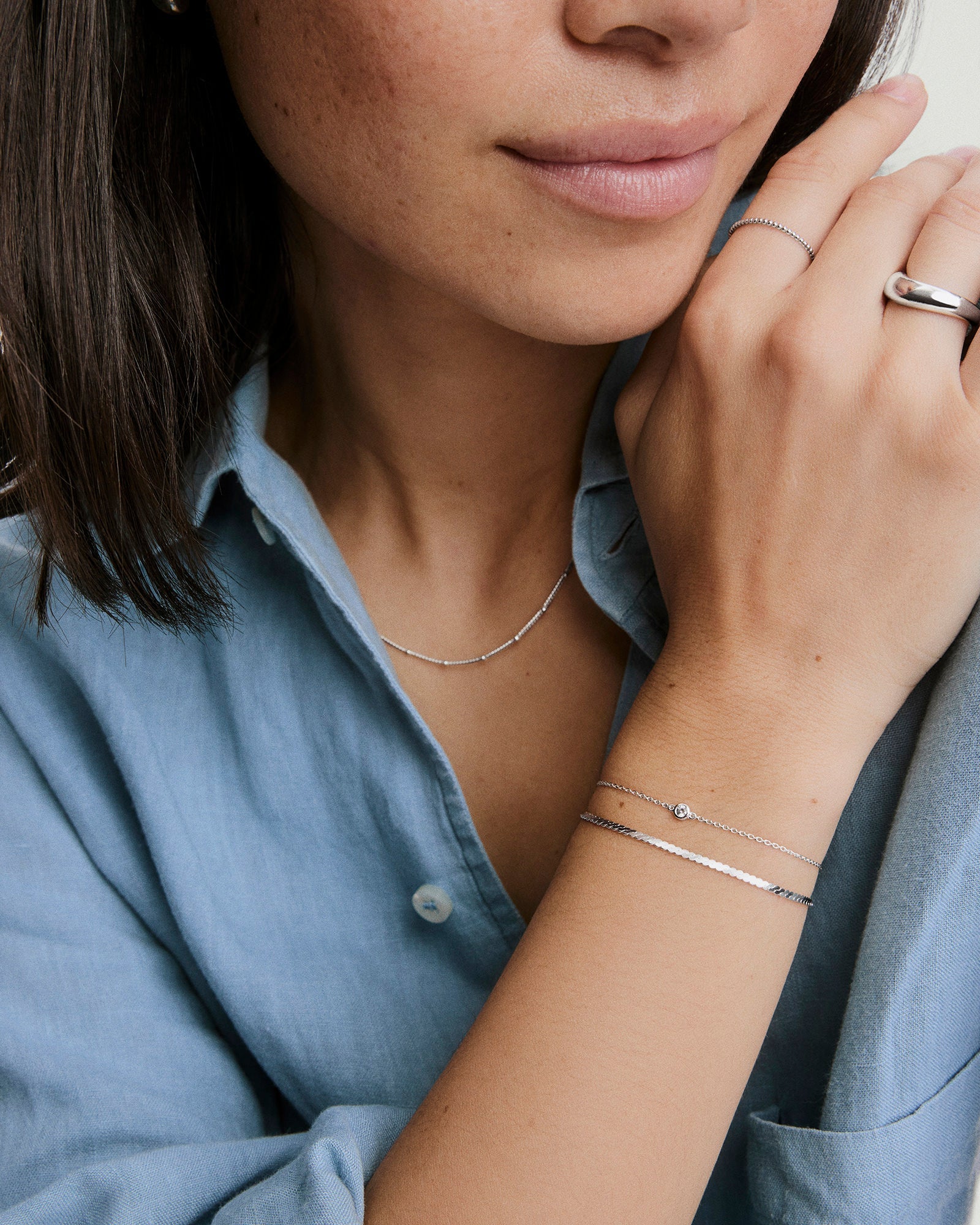 Young woman wearing the Double Take Bracelet Bundle, featuring a simple chain with a gemstone and a thin, flat-link silver bracelet on her wrist.