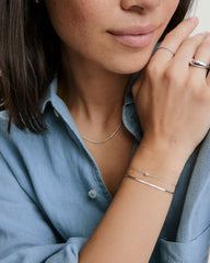 Young woman wearing the Double Take Bracelet Bundle, featuring a simple chain with a gemstone and a thin, flat-link silver bracelet on her wrist.