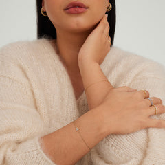 Woman wearing a white sweater showcases the Lotus Bracelet, a versatile gold accessory, elegantly highlighted among other gold jewelry pieces.