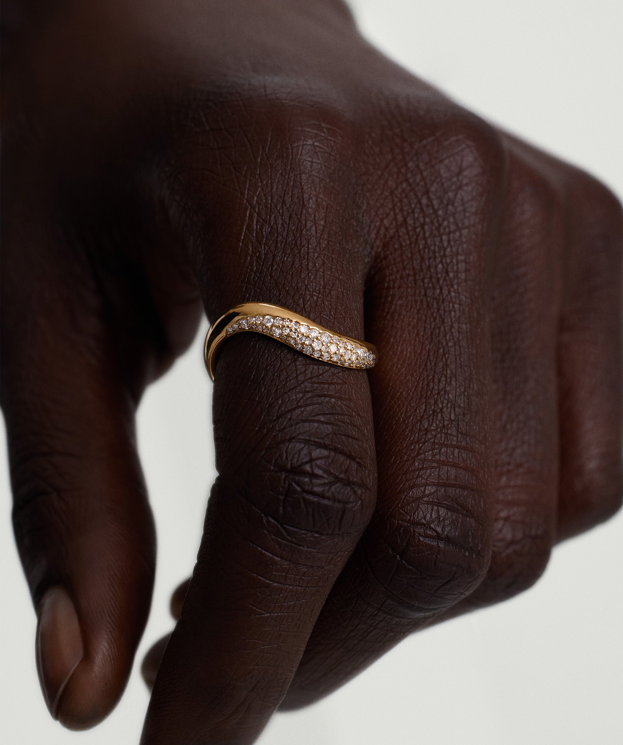 Close-up of a hand wearing the DÃ´me Figure Diamond Dipped Ring, featuring sleek curves, 14k gold, and pavÃ© diamonds.