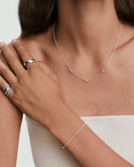 Person wearing a Floating Lab Grown Sapphire Necklace with three accents, silver rings on left hand, and a minimalist bracelet, against a bare-shouldered background.