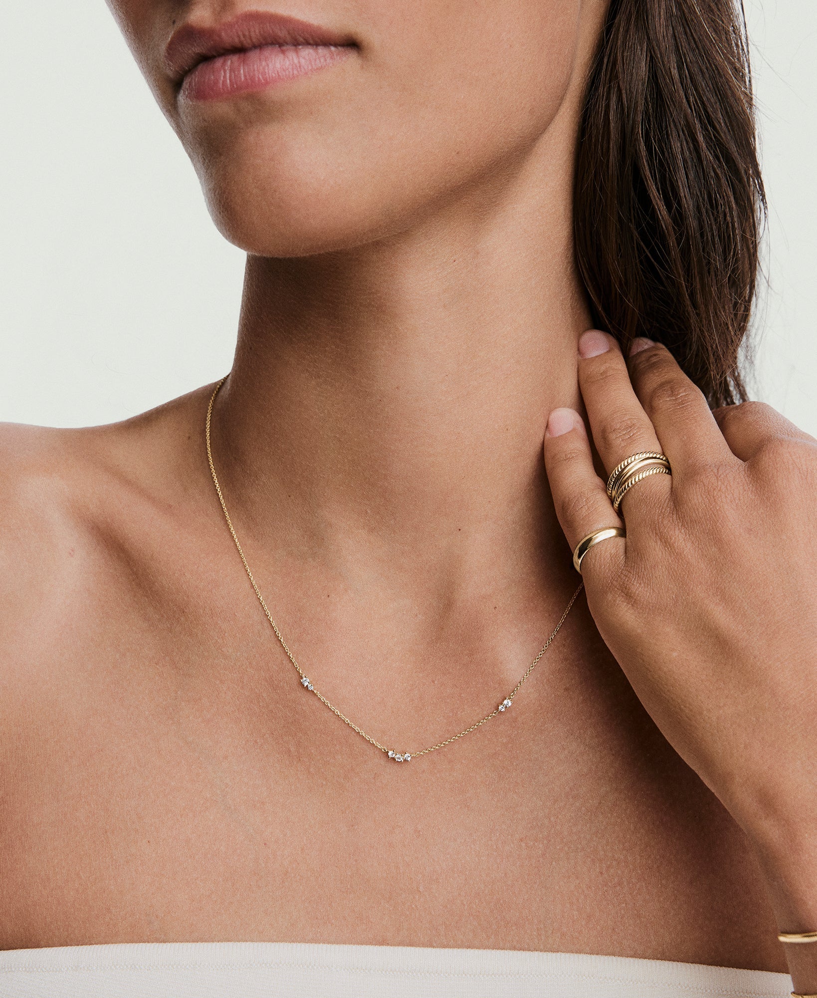 Close-up of a woman wearing the Floating Lab Grown Sapphire Necklace with three gemstone clusters, accompanied by gold rings on her hand near her collarbone.