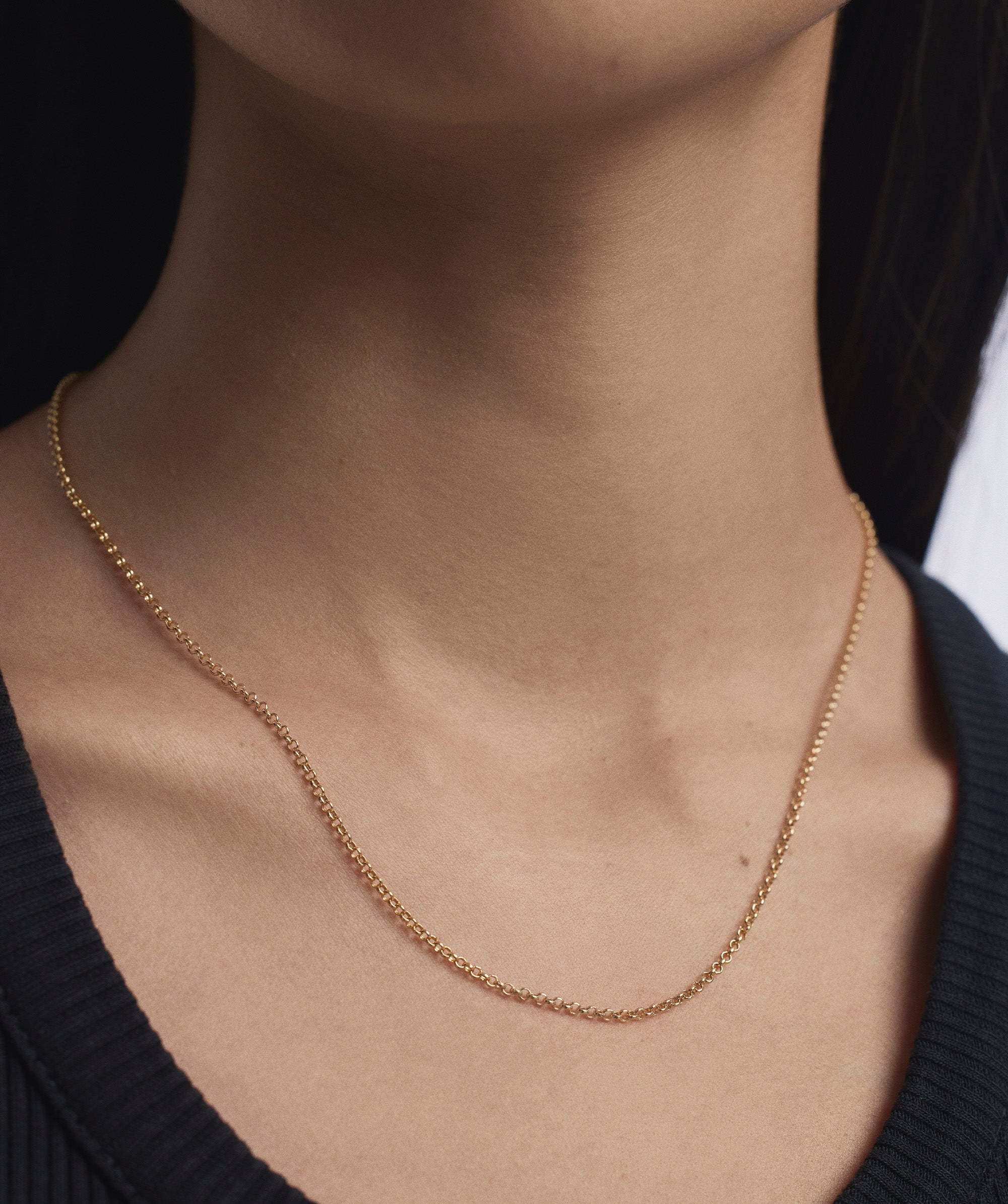 Woman wearing Baby Rolo Chain necklace, a minimalist gold chain designed for everyday wear, highlighted against a black shirt backdrop.