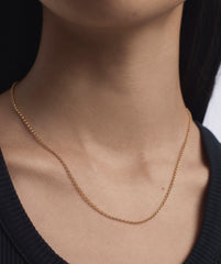 Woman wearing Baby Rolo Chain necklace, a minimalist gold chain designed for everyday wear, highlighted against a black shirt backdrop.