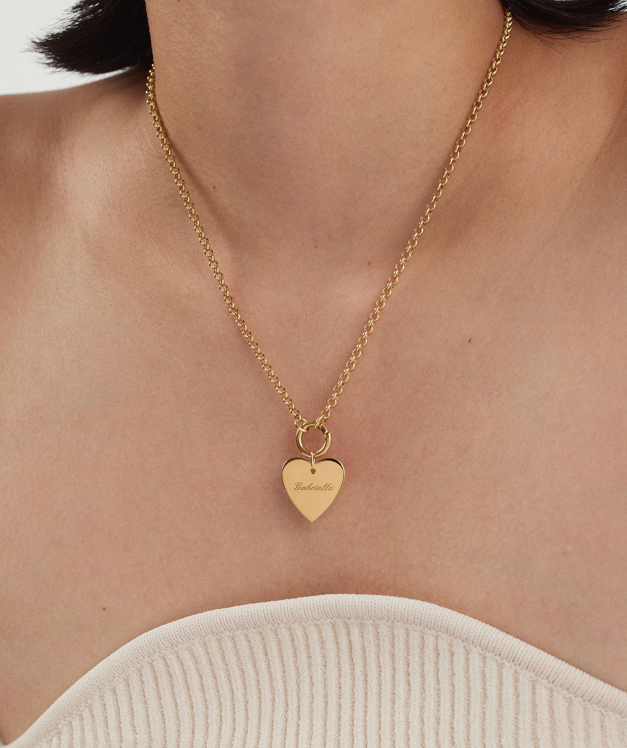 Person wearing a Flat Heart Charm necklace, featuring a gold heart-shaped pendant engraved with a name, adding a romantic touch to their ensemble.
