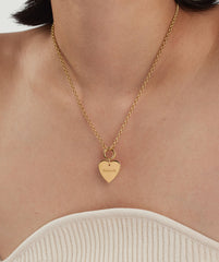 Person wearing a Flat Heart Charm necklace, featuring a gold heart-shaped pendant engraved with a name, adding a romantic touch to their ensemble.