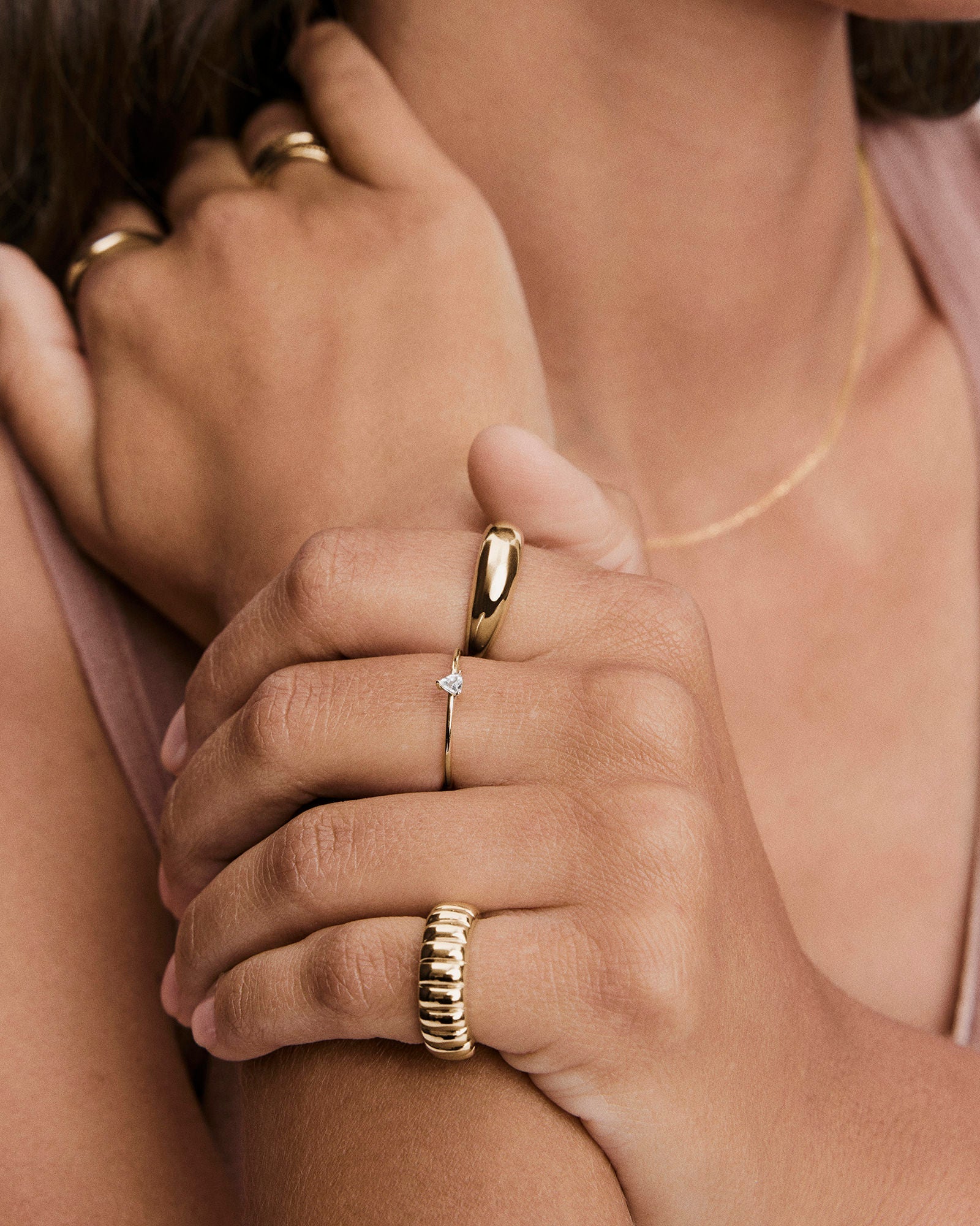 Hands adorned with gold jewelry, highlighting the Gemstone Trillion Stacker Ring on the ring finger, featuring a slender band and heart-shaped topaz gemstone.