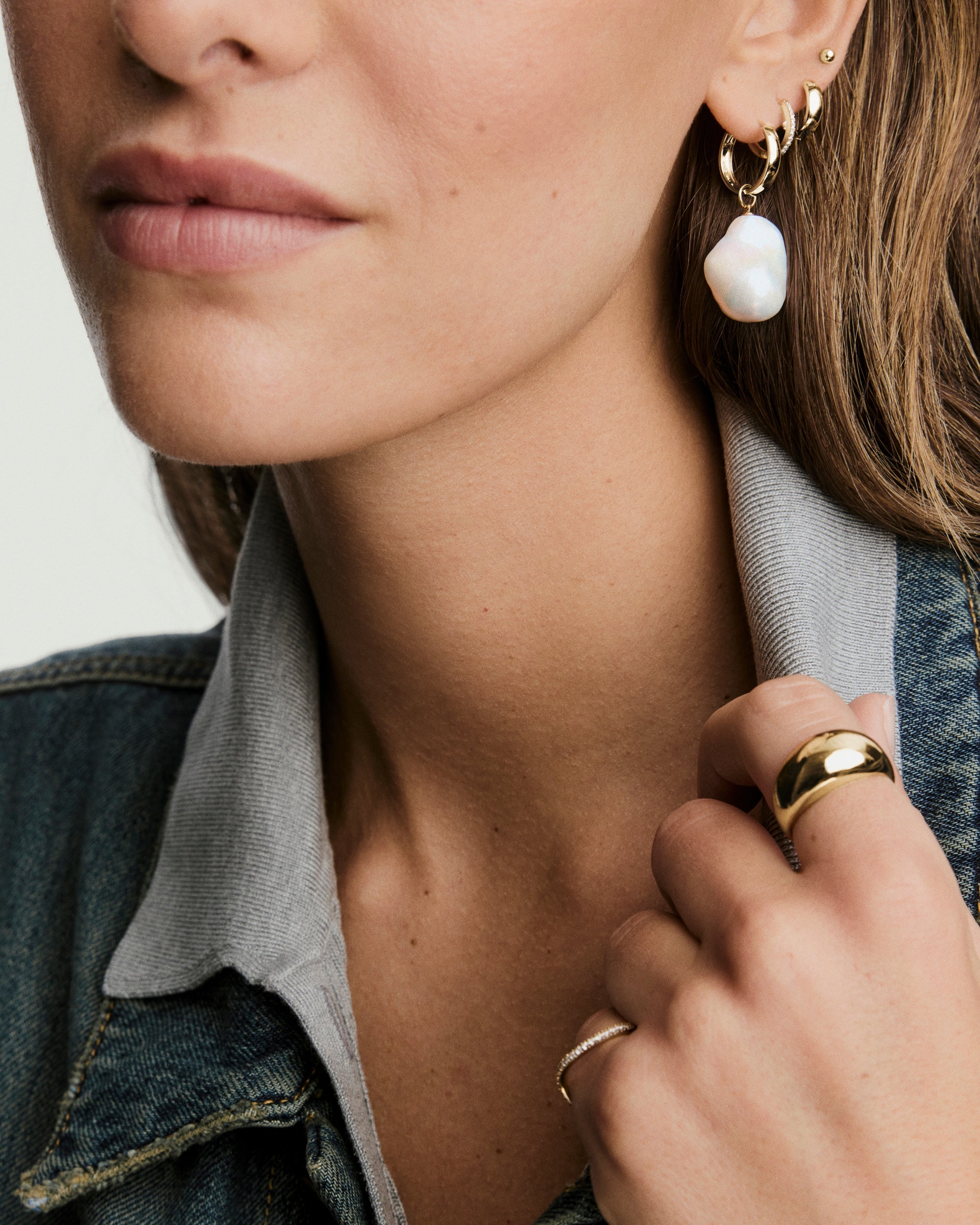 Close-up of a woman's ear showcasing an Oversized Baroque Pearl Hoop Charm, highlighting its irregular, sculptural shape paired with gold hoop earrings.