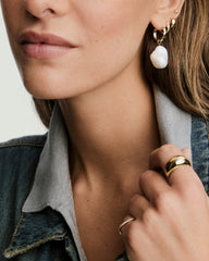 Close-up of a woman's ear showcasing an Oversized Baroque Pearl Hoop Charm, highlighting its irregular, sculptural shape paired with gold hoop earrings.