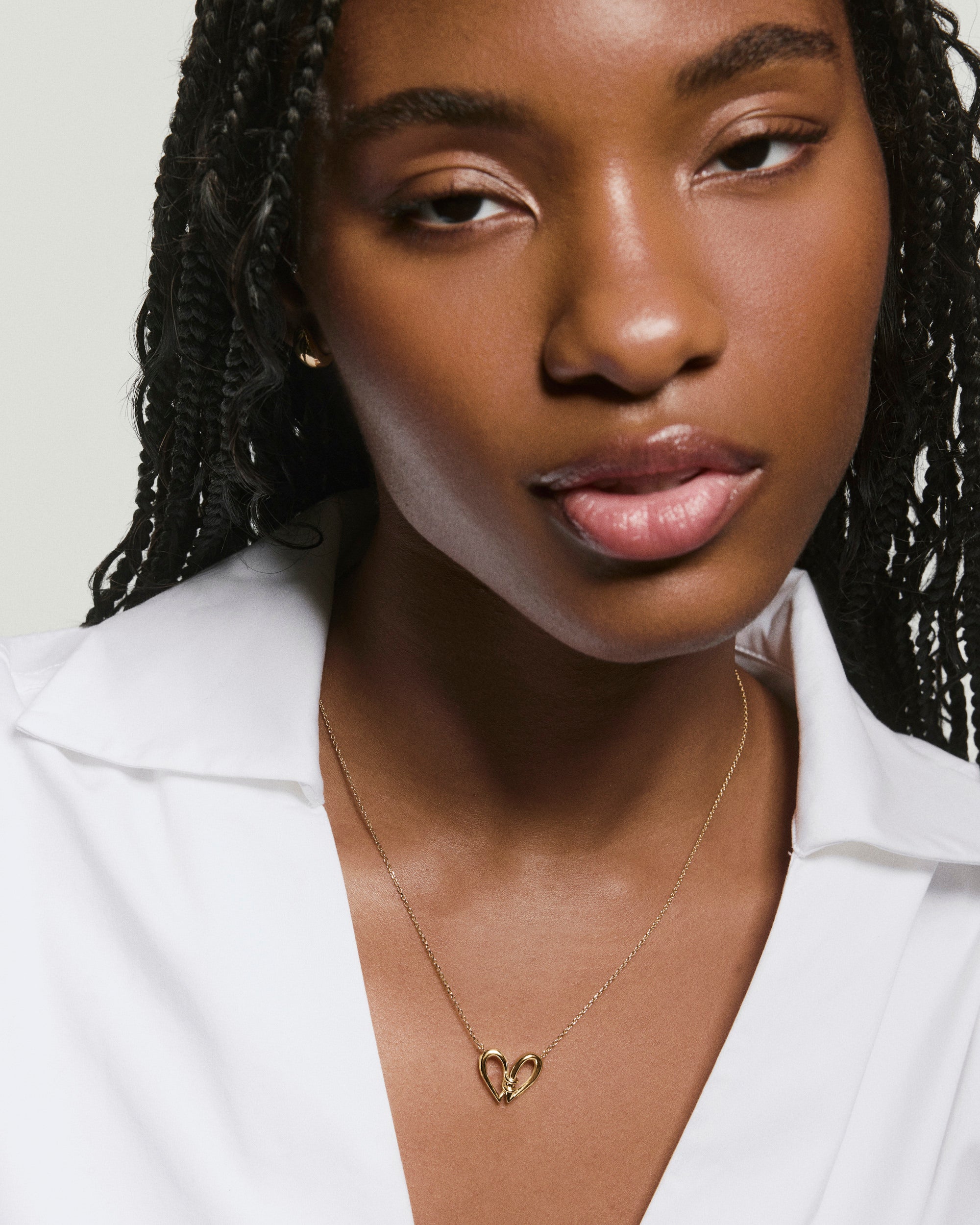 Heart to Heart Necklace on a womanâs neck, featuring two gold sculptural drops forming a modern heart, worn over a white collared shirt.
