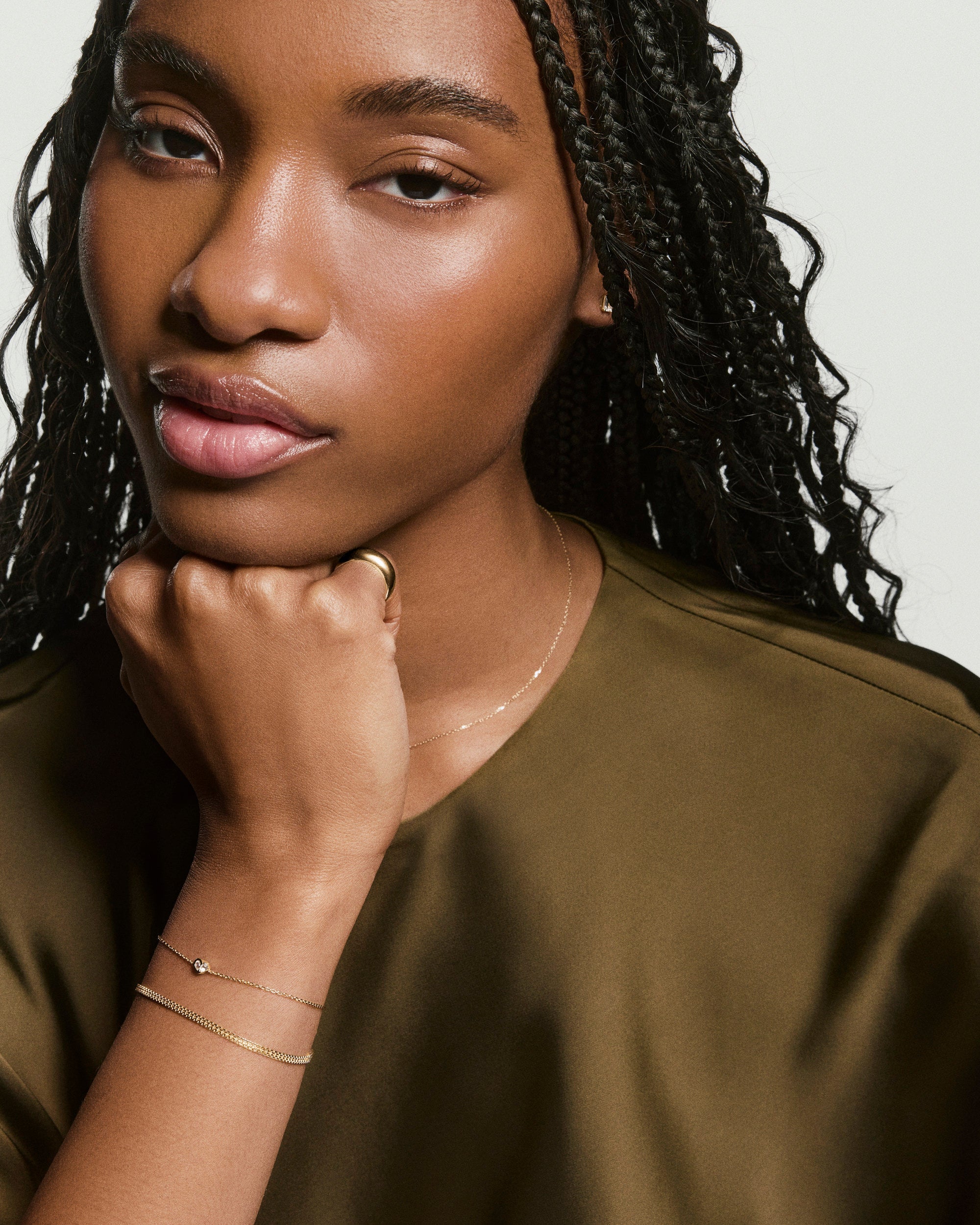 Young woman wears the Two of Hearts Bracelet, featuring delicate gold design with a tiny stone, enhancing her stylish look with understated elegance.