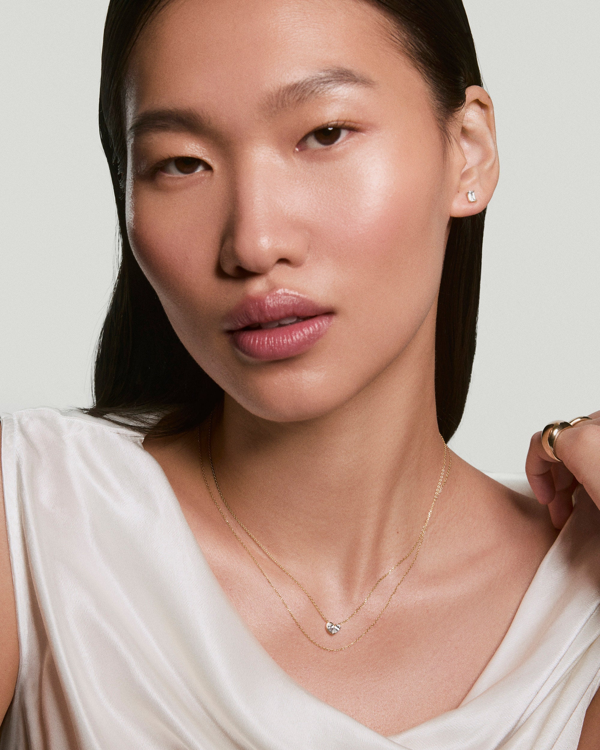 Woman wearing Two of Hearts Necklace, featuring a heart-shaped pendant on a fine gold chain, paired with square stud earrings and a chunky ring.