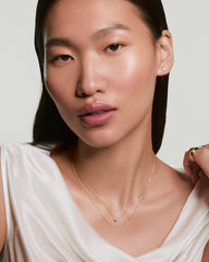 Woman wearing Two of Hearts Necklace, featuring a heart-shaped pendant on a fine gold chain, paired with square stud earrings and a chunky ring.