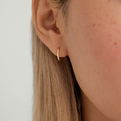 Close-up of a woman's ear wearing Easy Huggie Hoops, handcrafted in 14k gold with a clicker closure for comfortable everyday wear.
