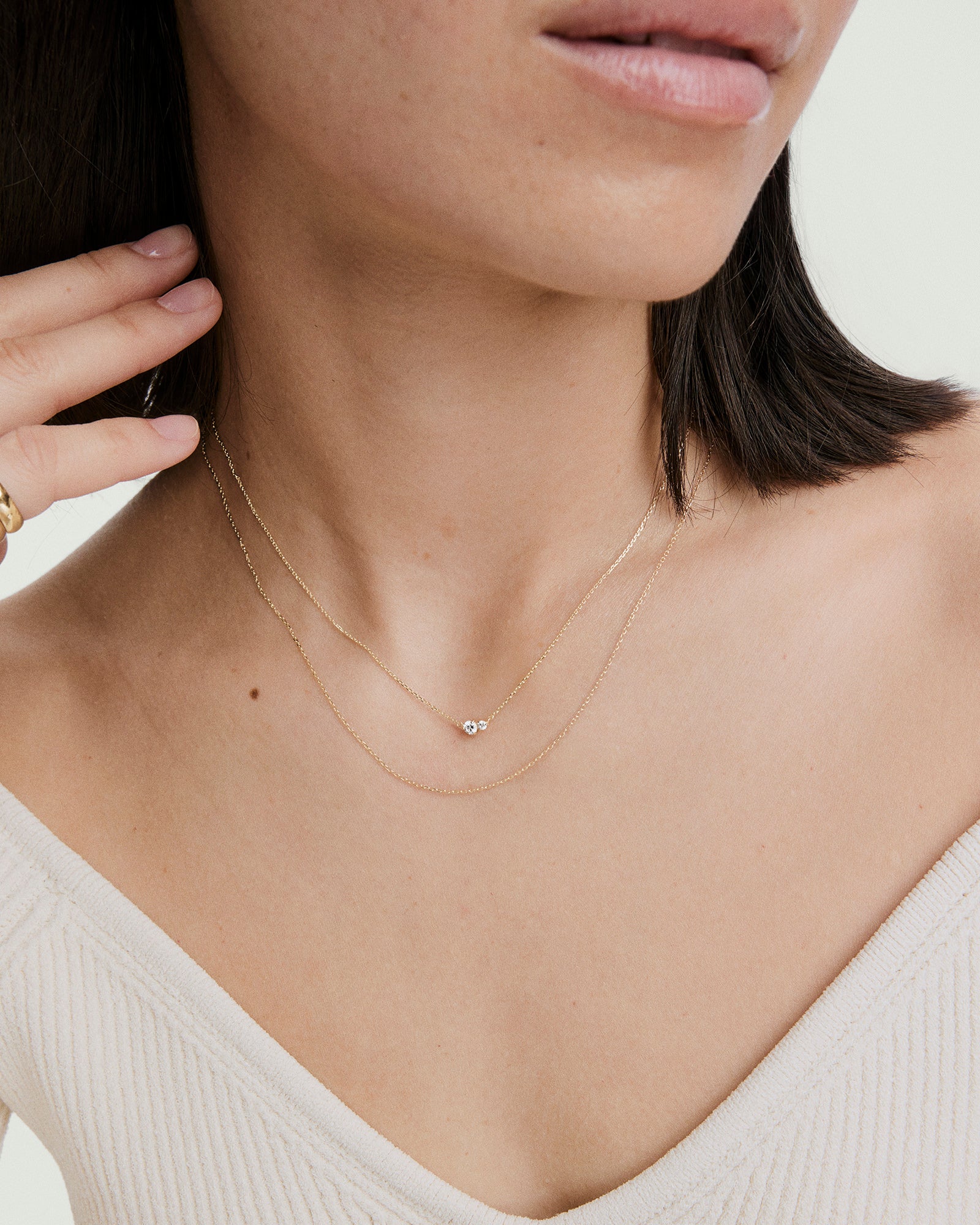 Woman wearing the Beverly Necklace: two layered gold chains with a small gemstone, complemented by a gold ring and rib-knit off-shoulder top.